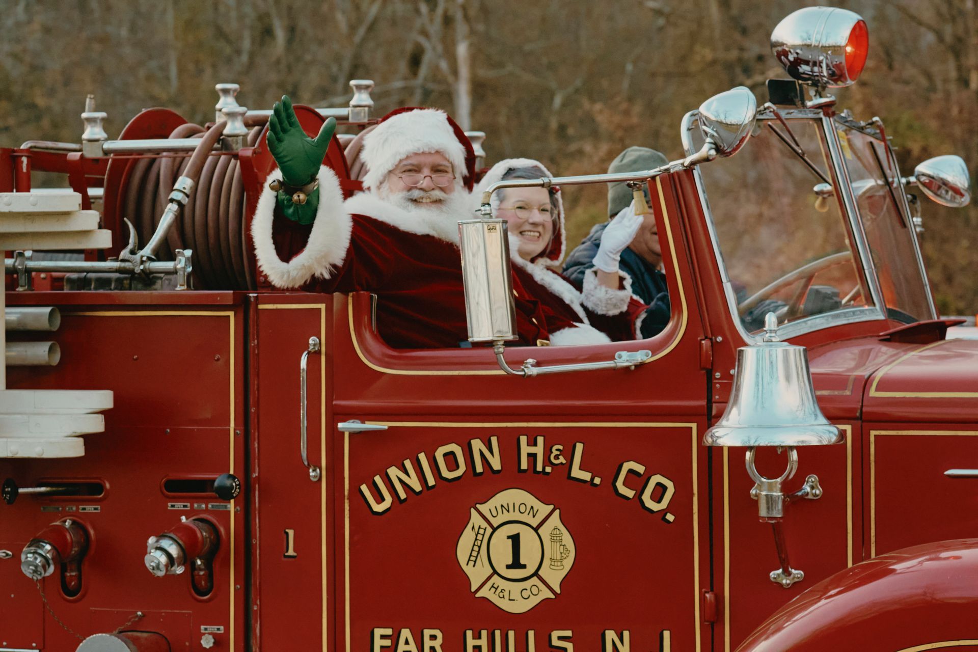 Santa Claus waves from a red fire truck. A woman is with him. 