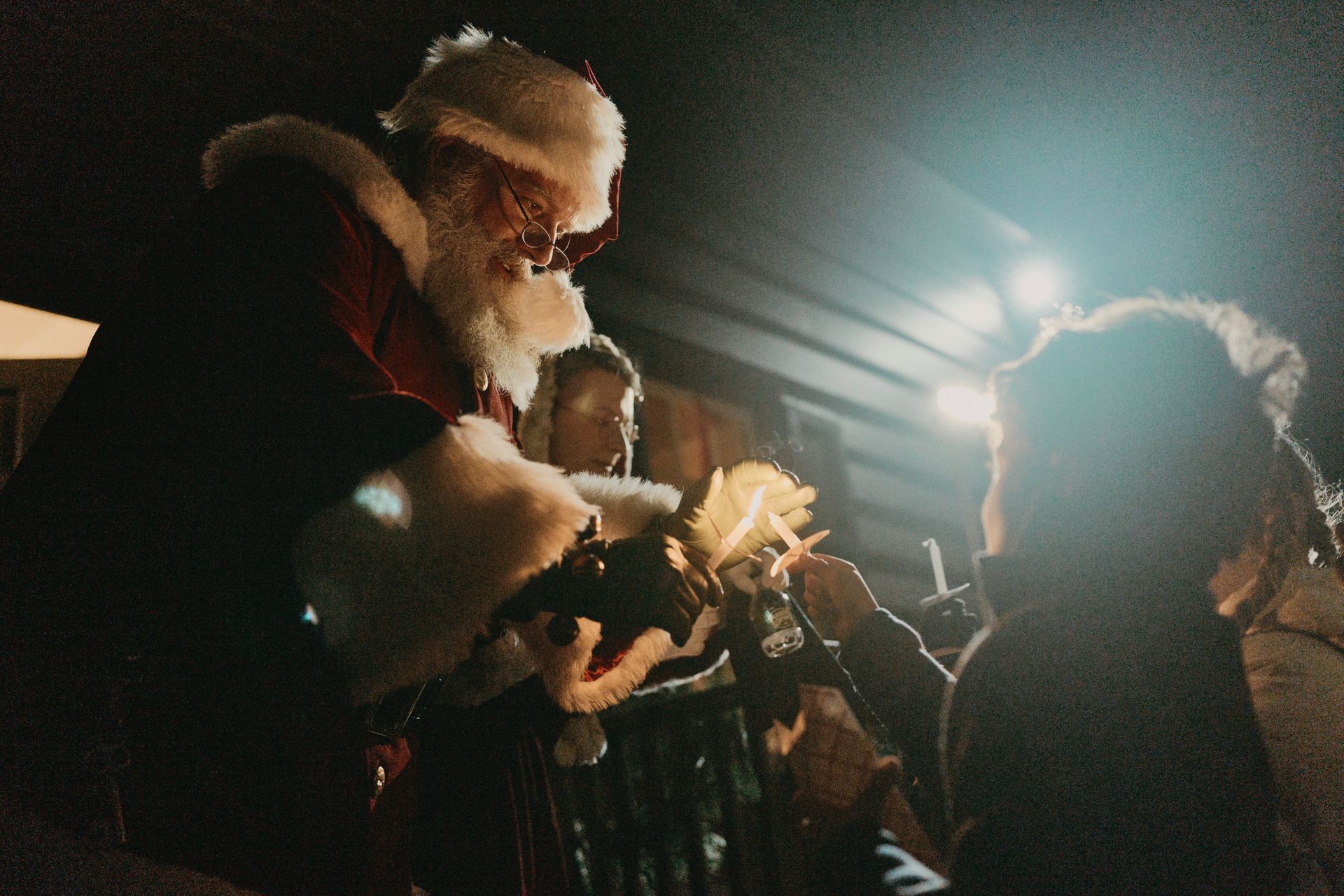 Santa Claus handing gifts to children outdoors at night.