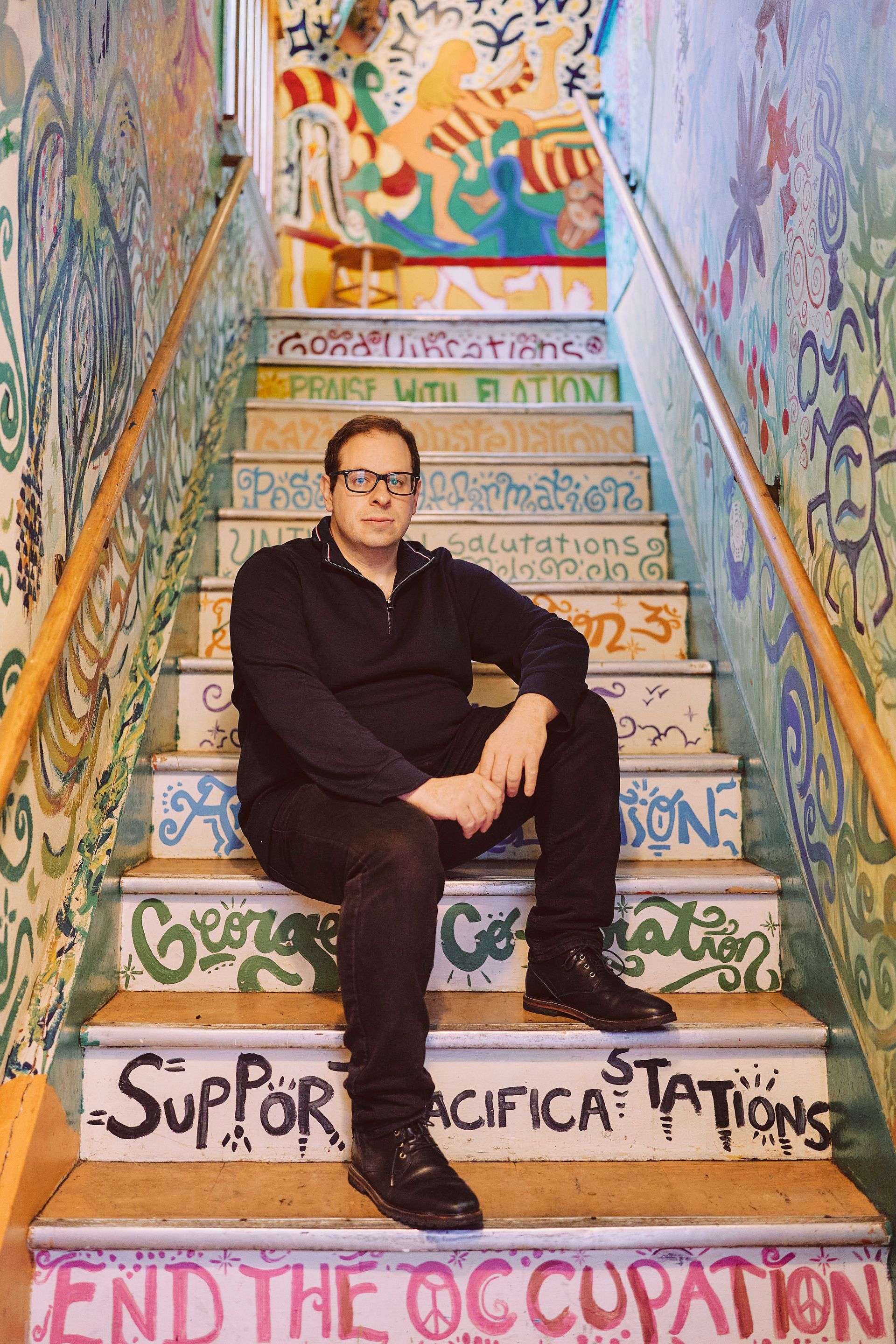Man seated on colorful staircase with painted messages.