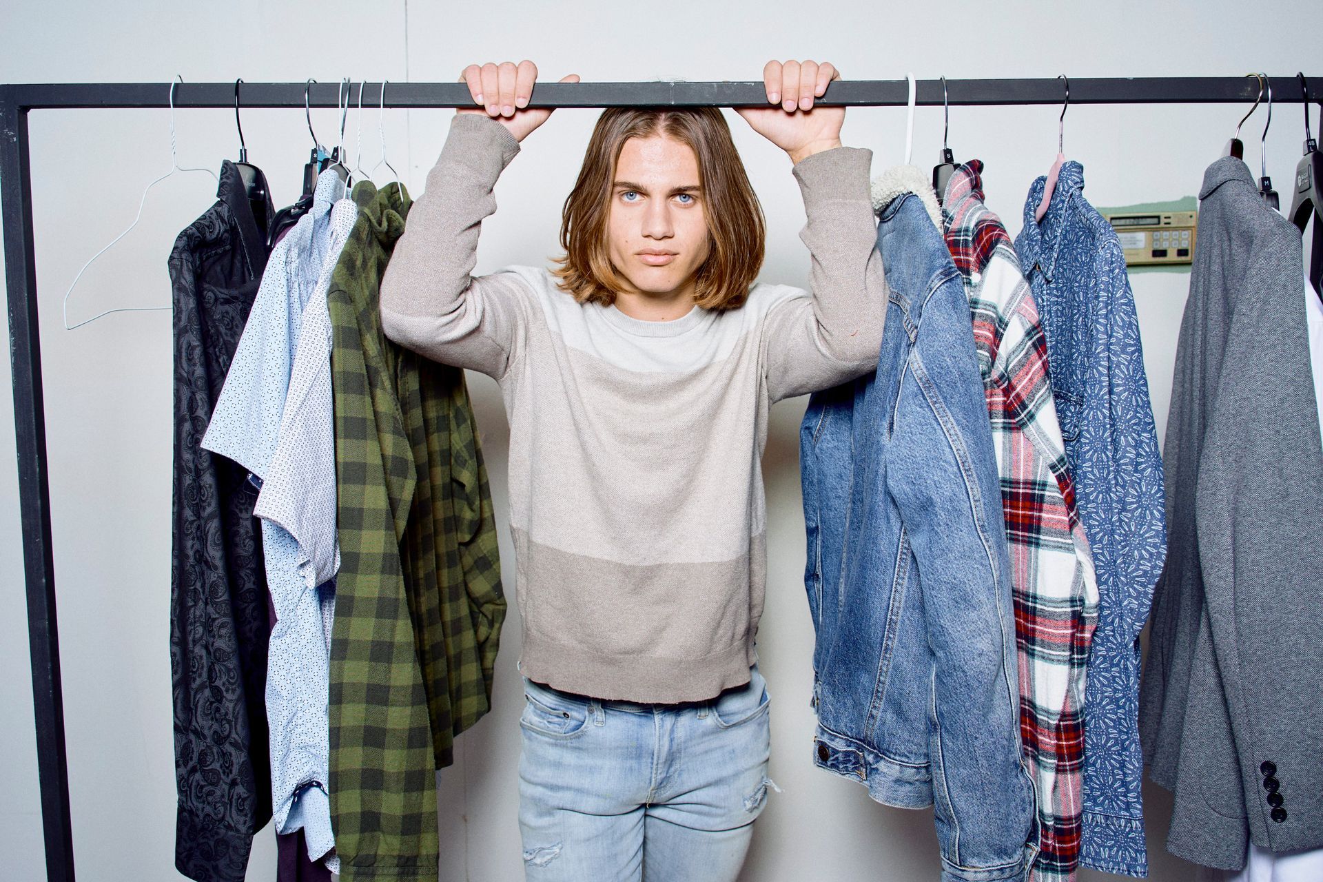 A young man is hanging on a rack of clothes.
