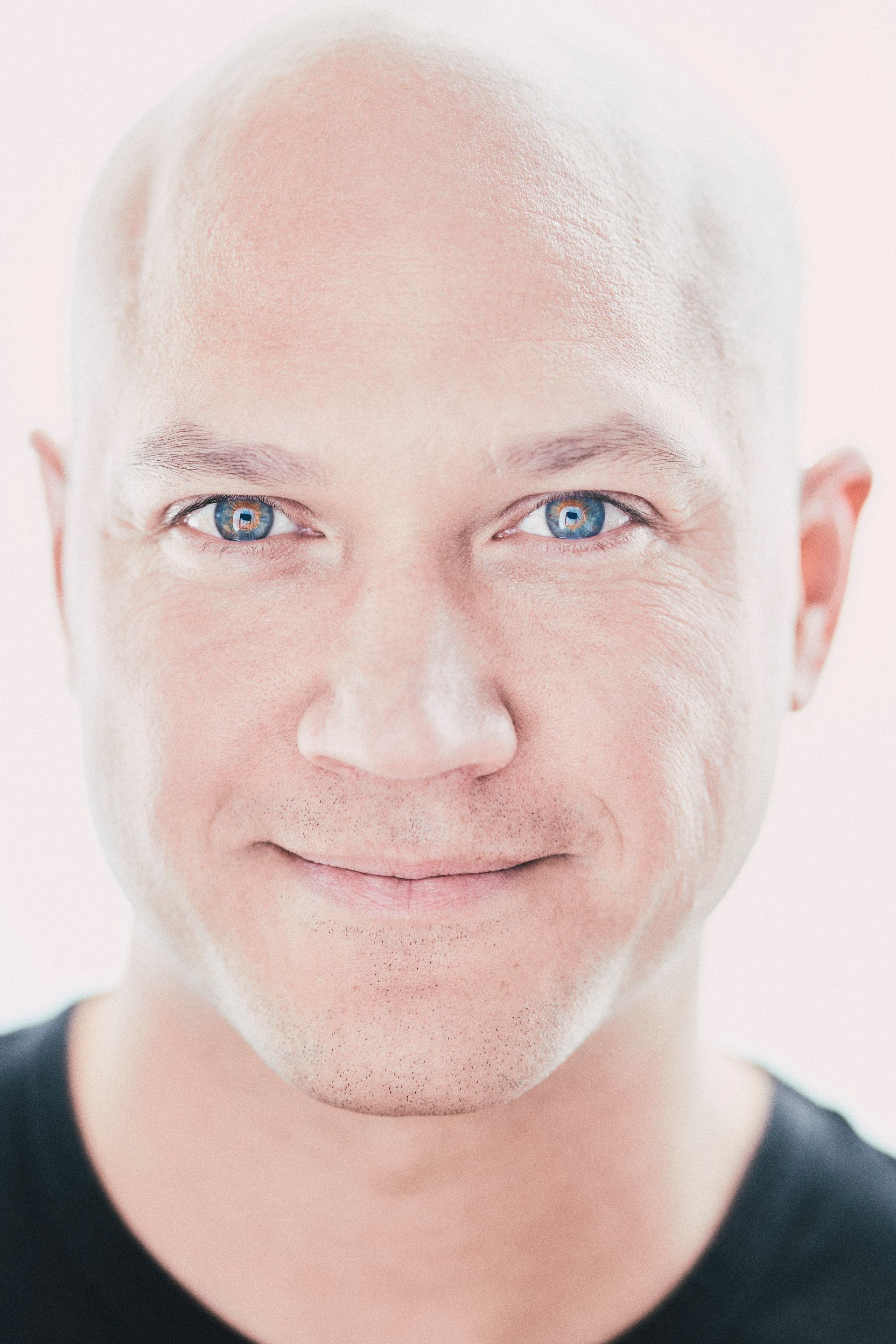 A close up of a bald man 's face with blue eyes and a black shirt.