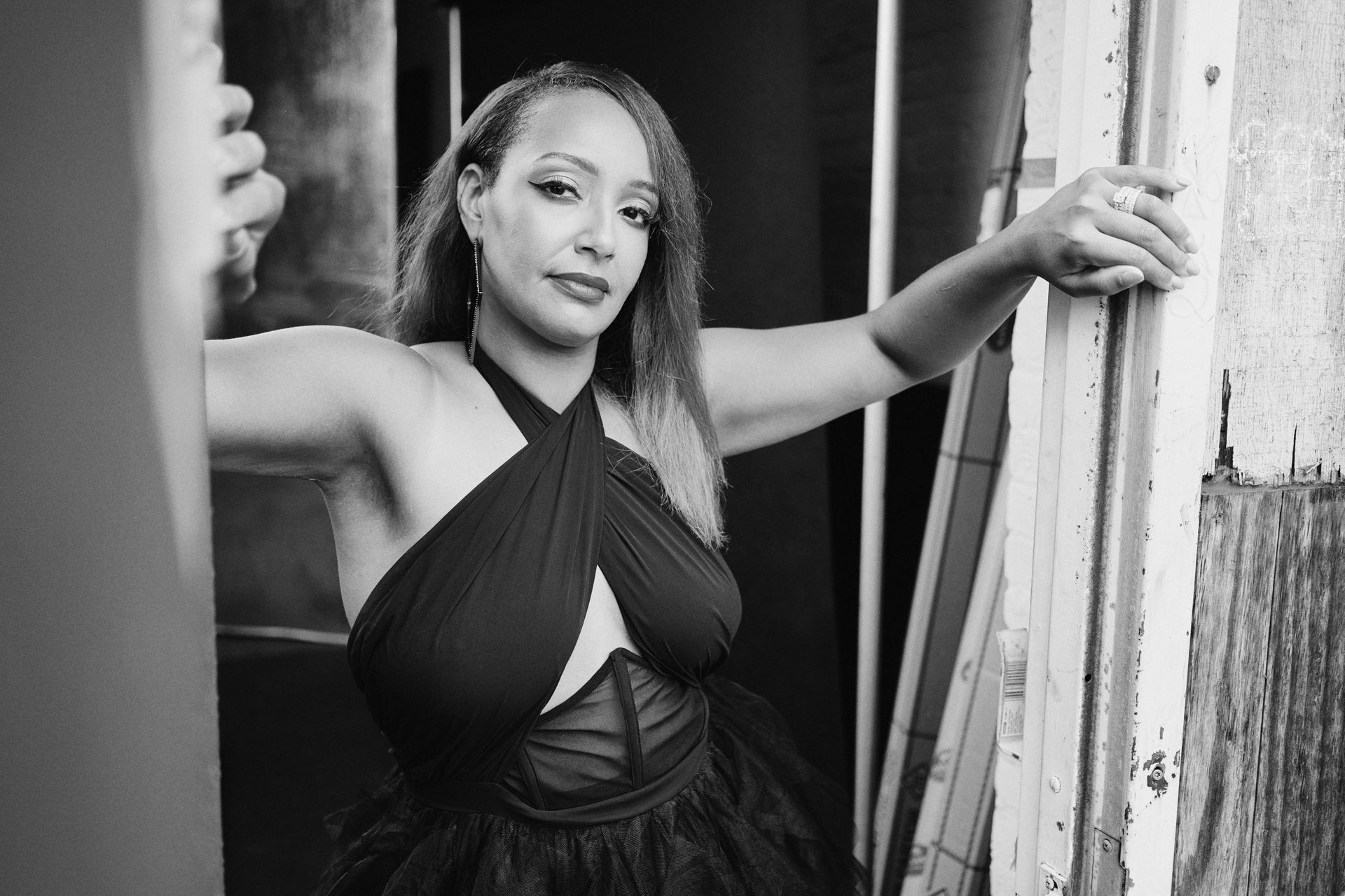A black and white photo of a woman in a dress leaning against a wall.