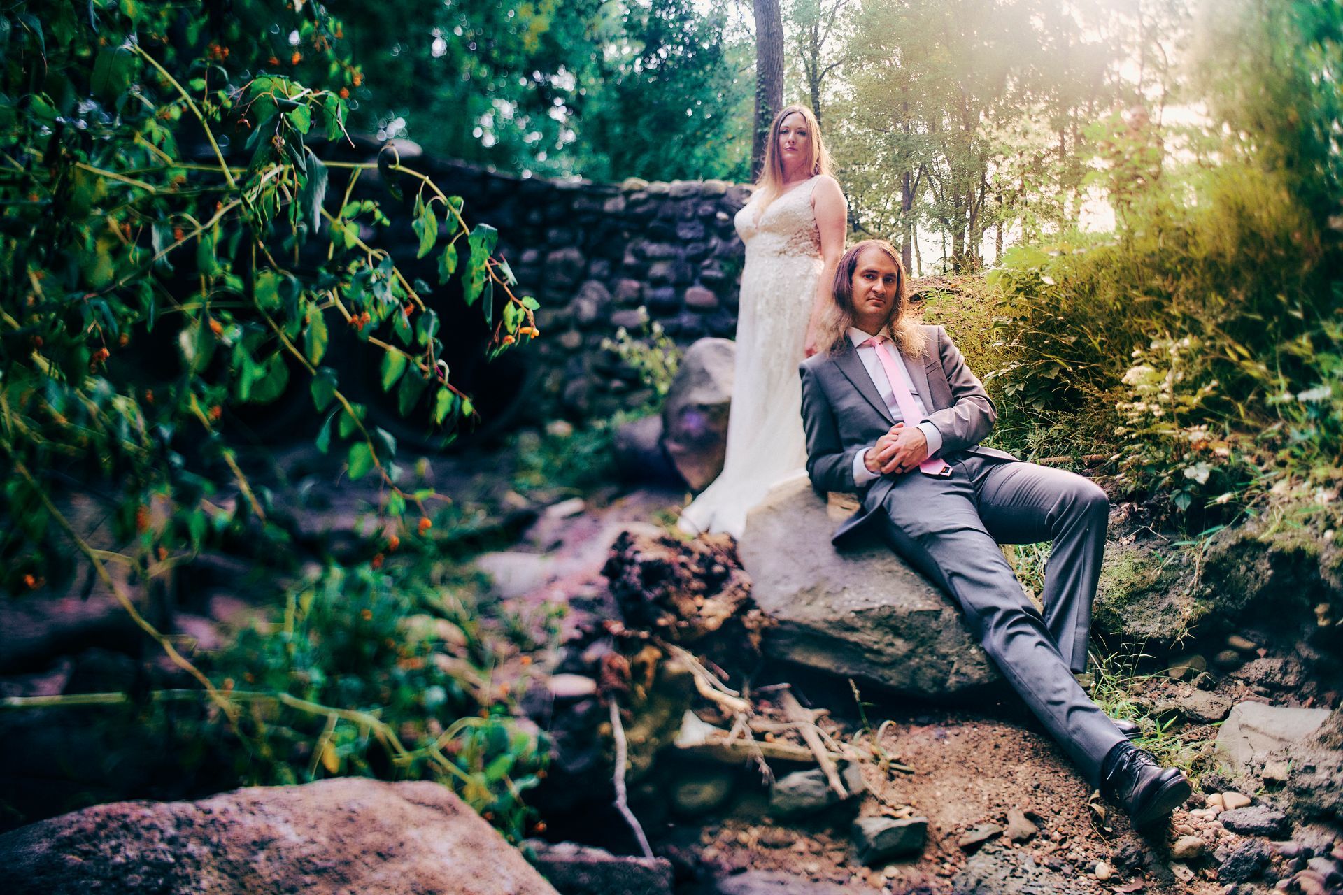 A bride and groom are sitting on a rock in the woods.