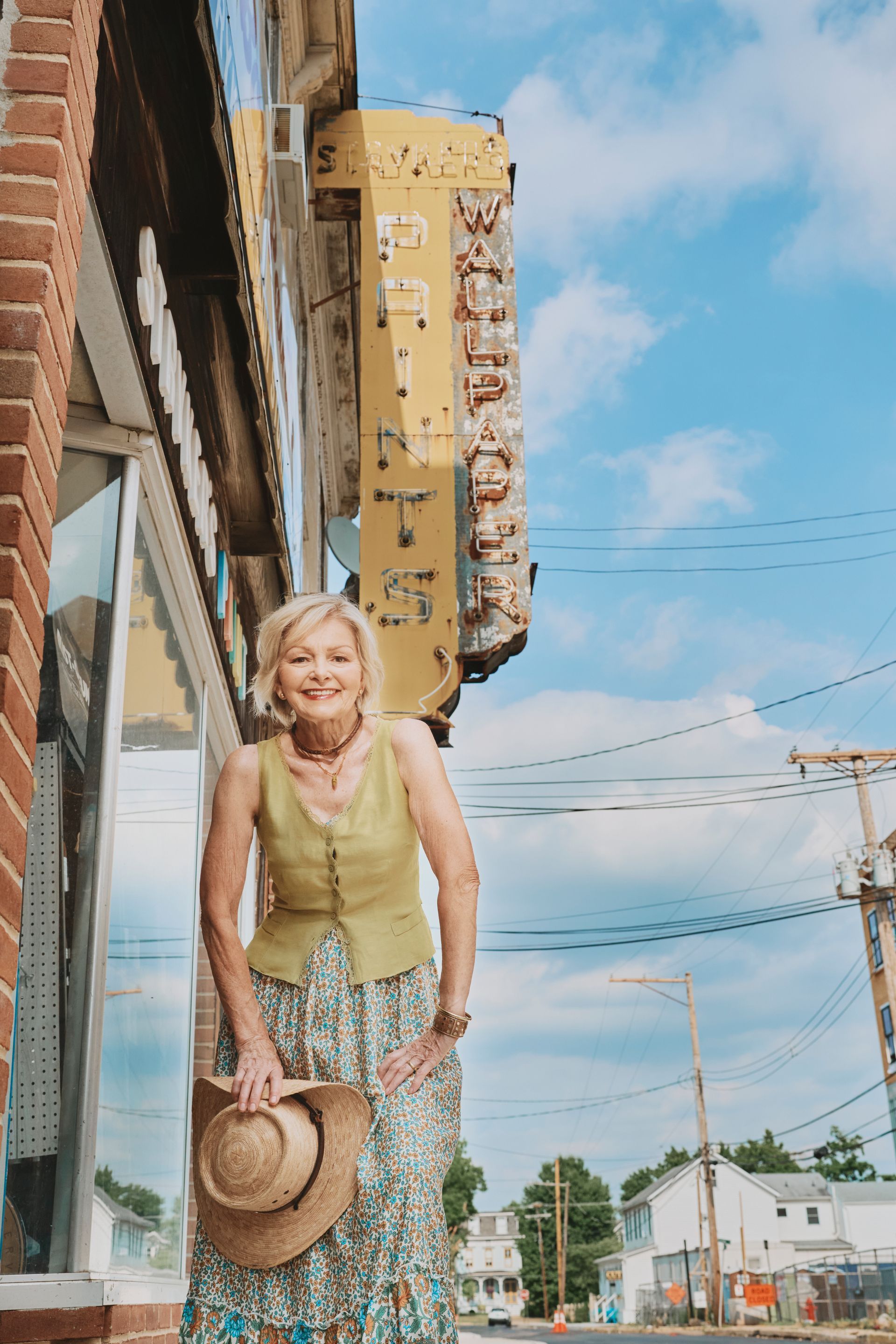 A woman is standing in front of a building holding a cowboy hat.