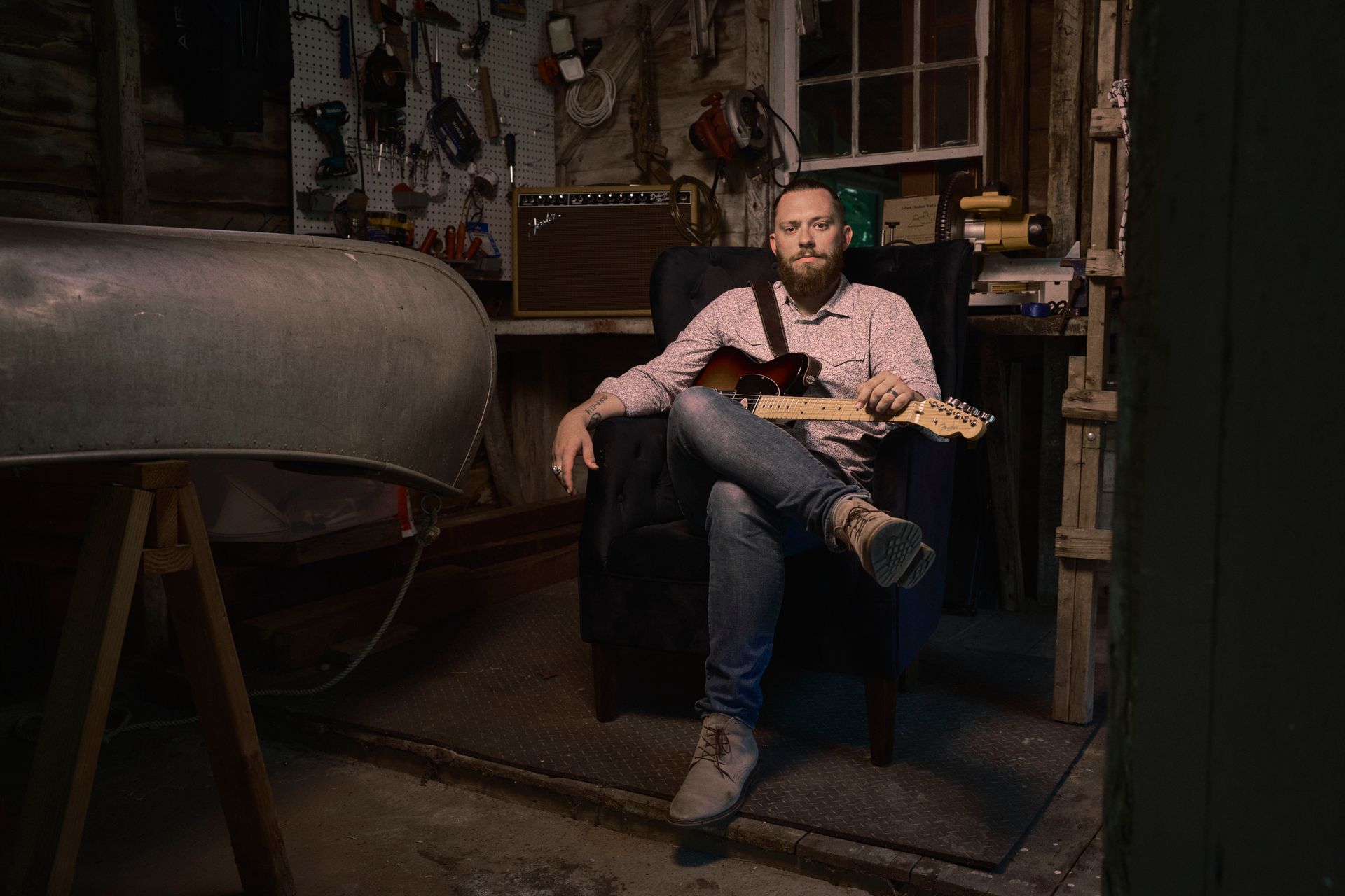 A man is sitting in a chair holding a guitar in a garage.