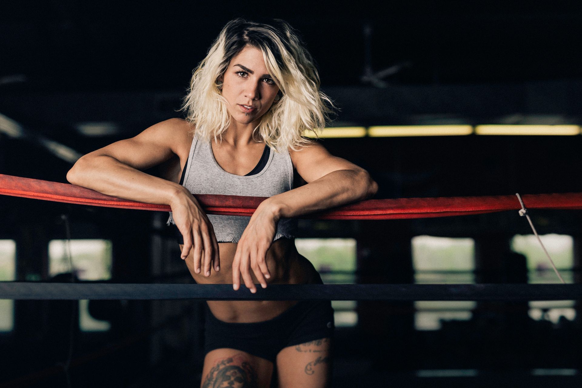 A woman is leaning against a boxing ring in a gym.