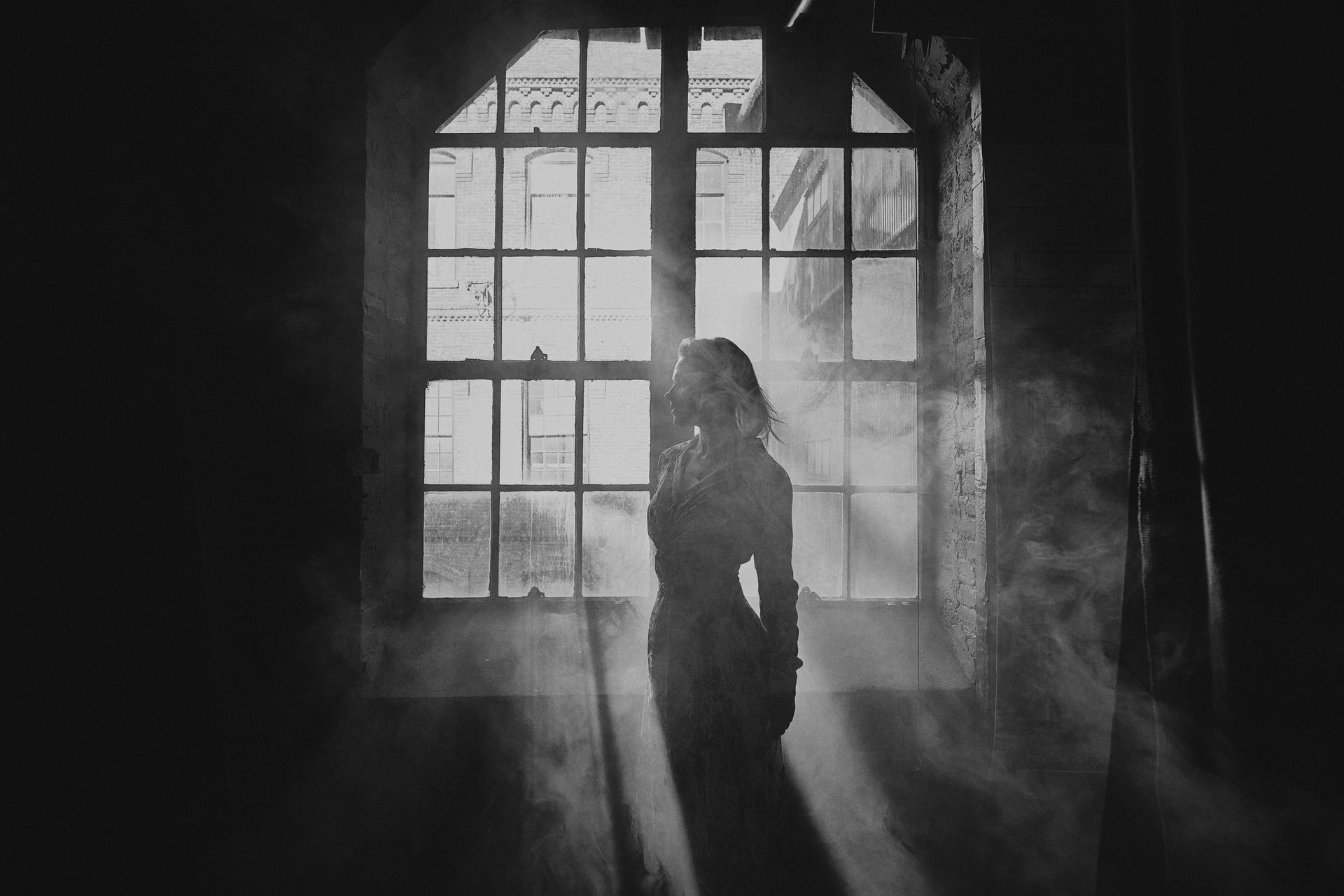 Silhouetted person standing before a bright window in a dark, smoky room