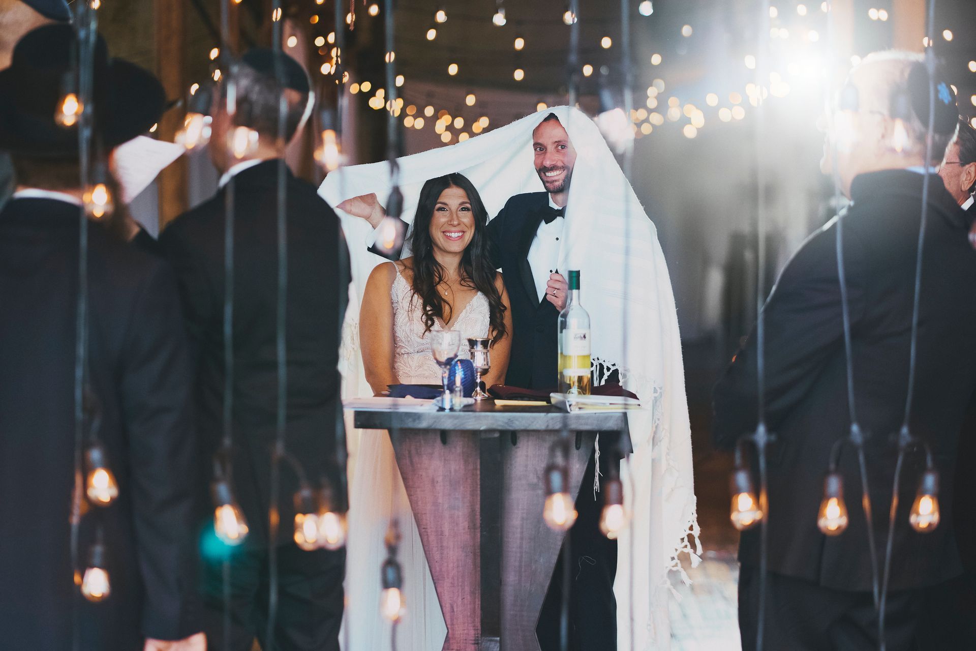 A bride and groom are sitting at a table under a blanket.