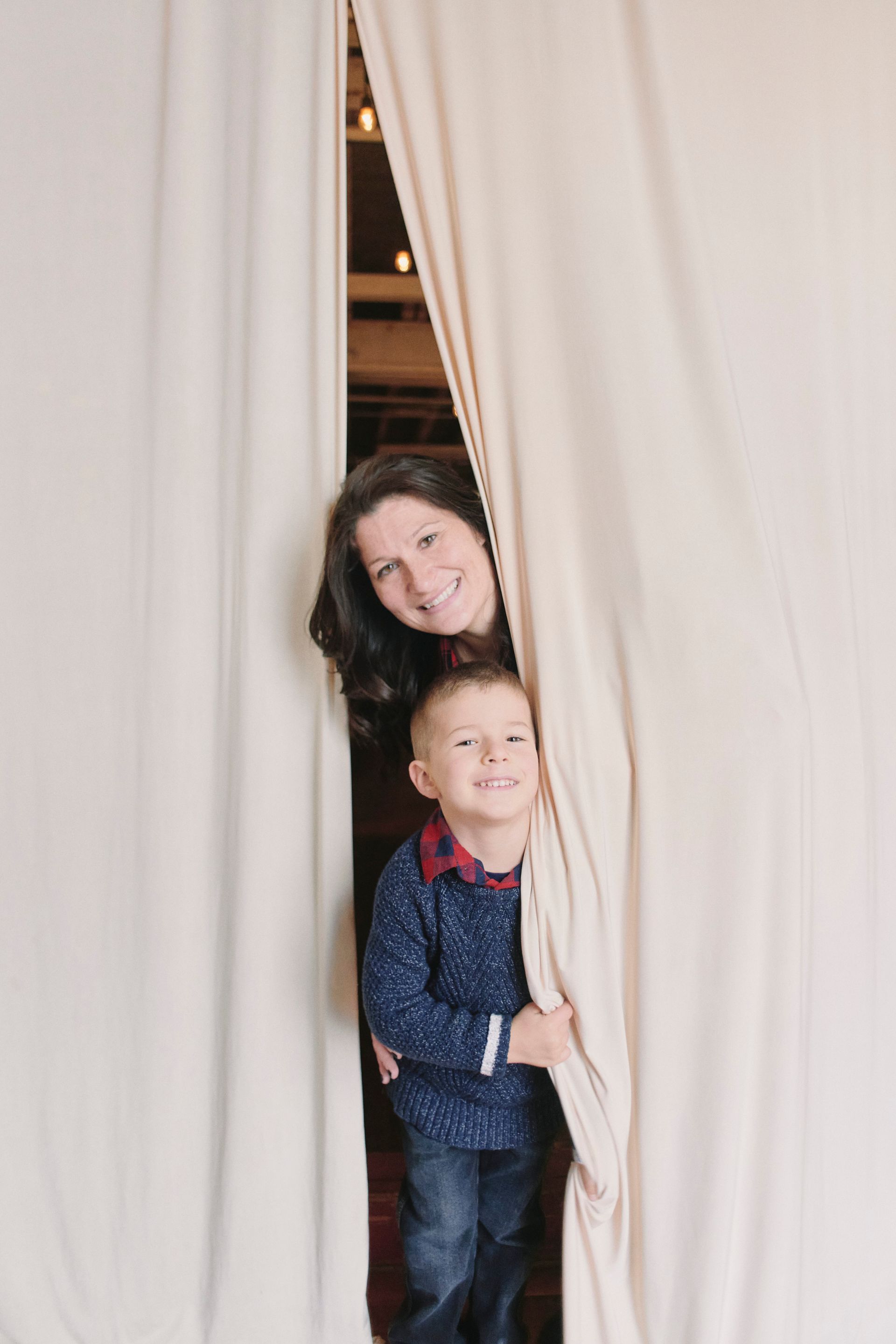 A woman and a child are peeking out from behind a curtain.