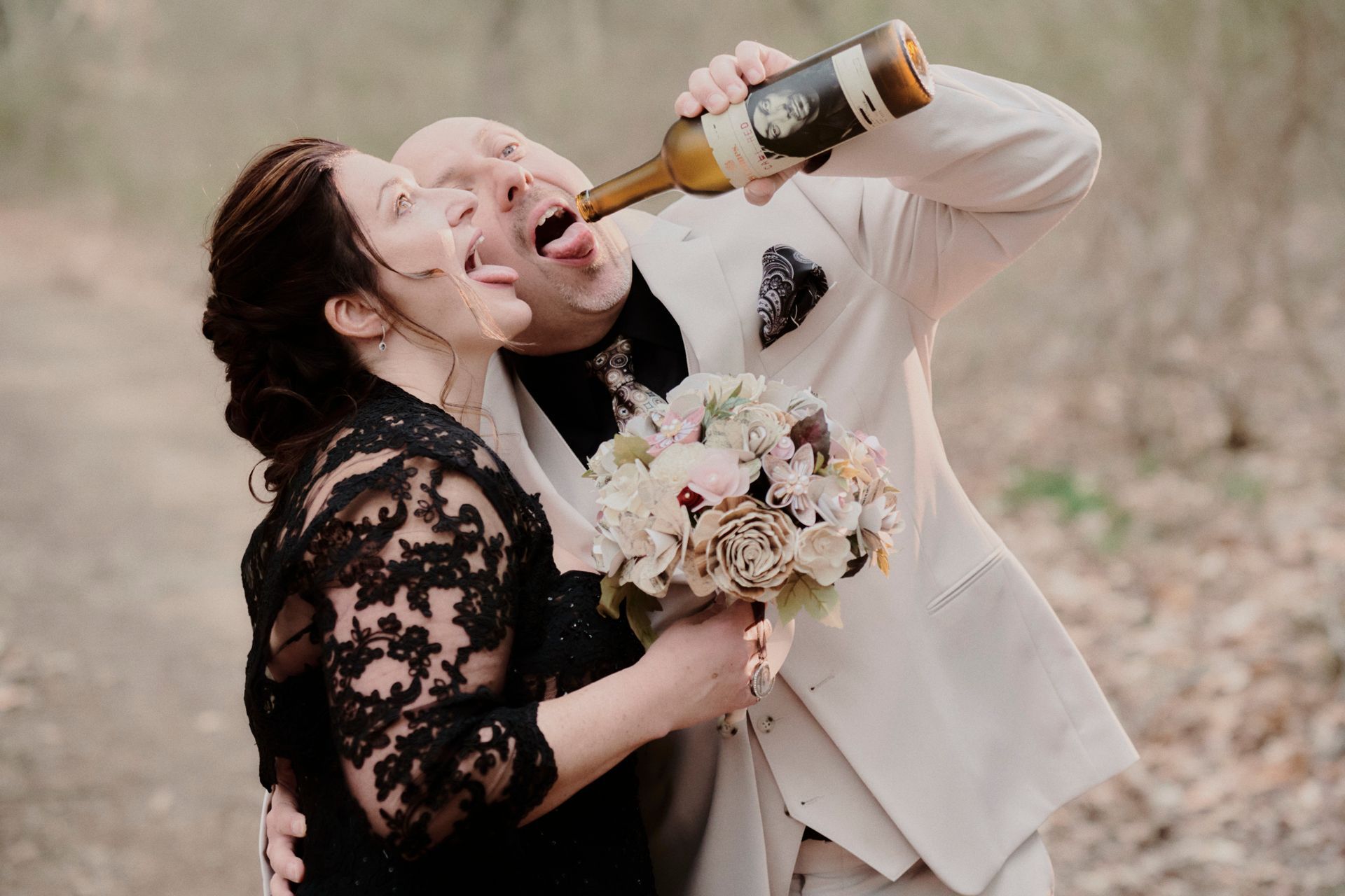 A bride and groom are drinking from a bottle of wine.