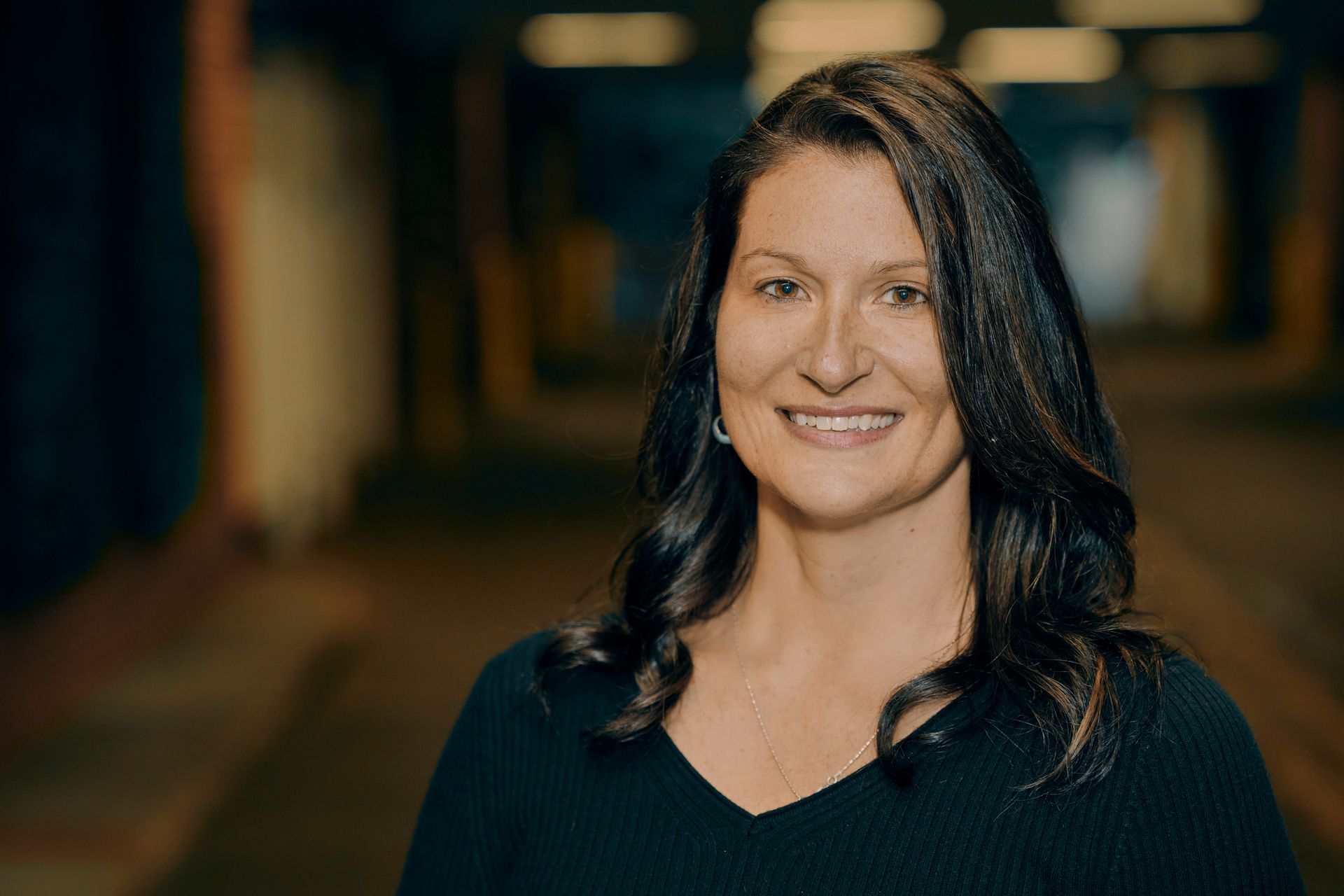 Woman with dark hair smiles, wearing a black top, in a tunnel setting.