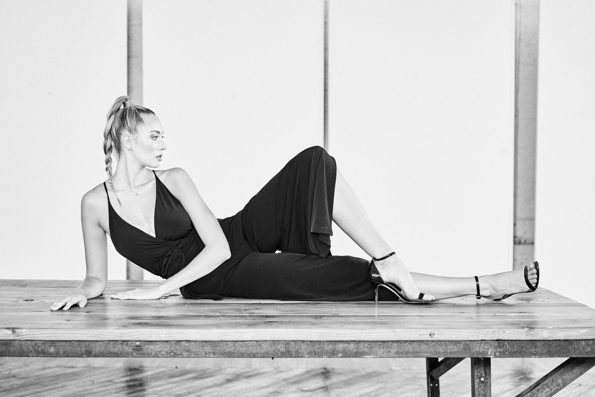 A woman in a black jumpsuit is laying on a wooden bench.