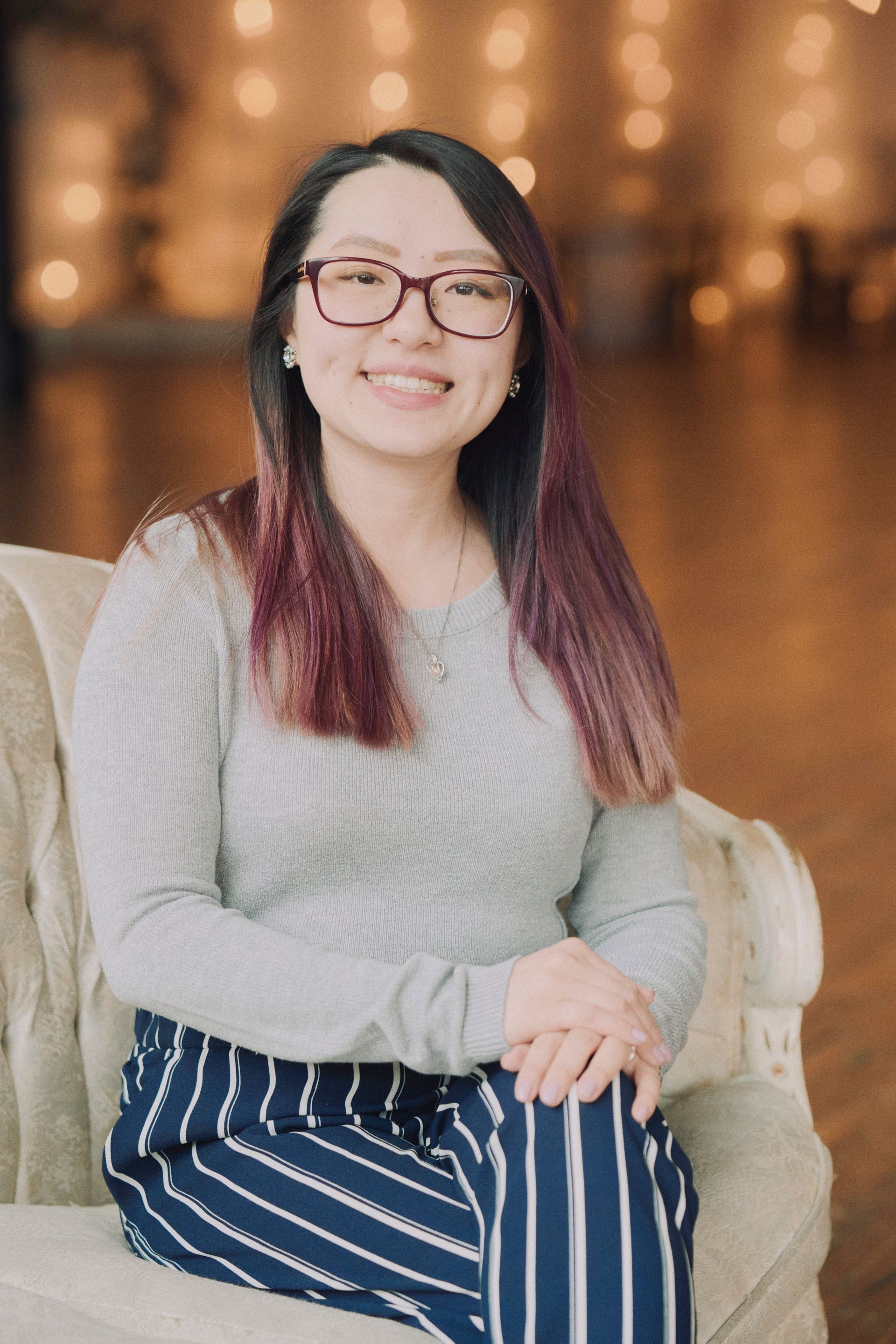A woman wearing glasses and striped pants is sitting in a chair.
