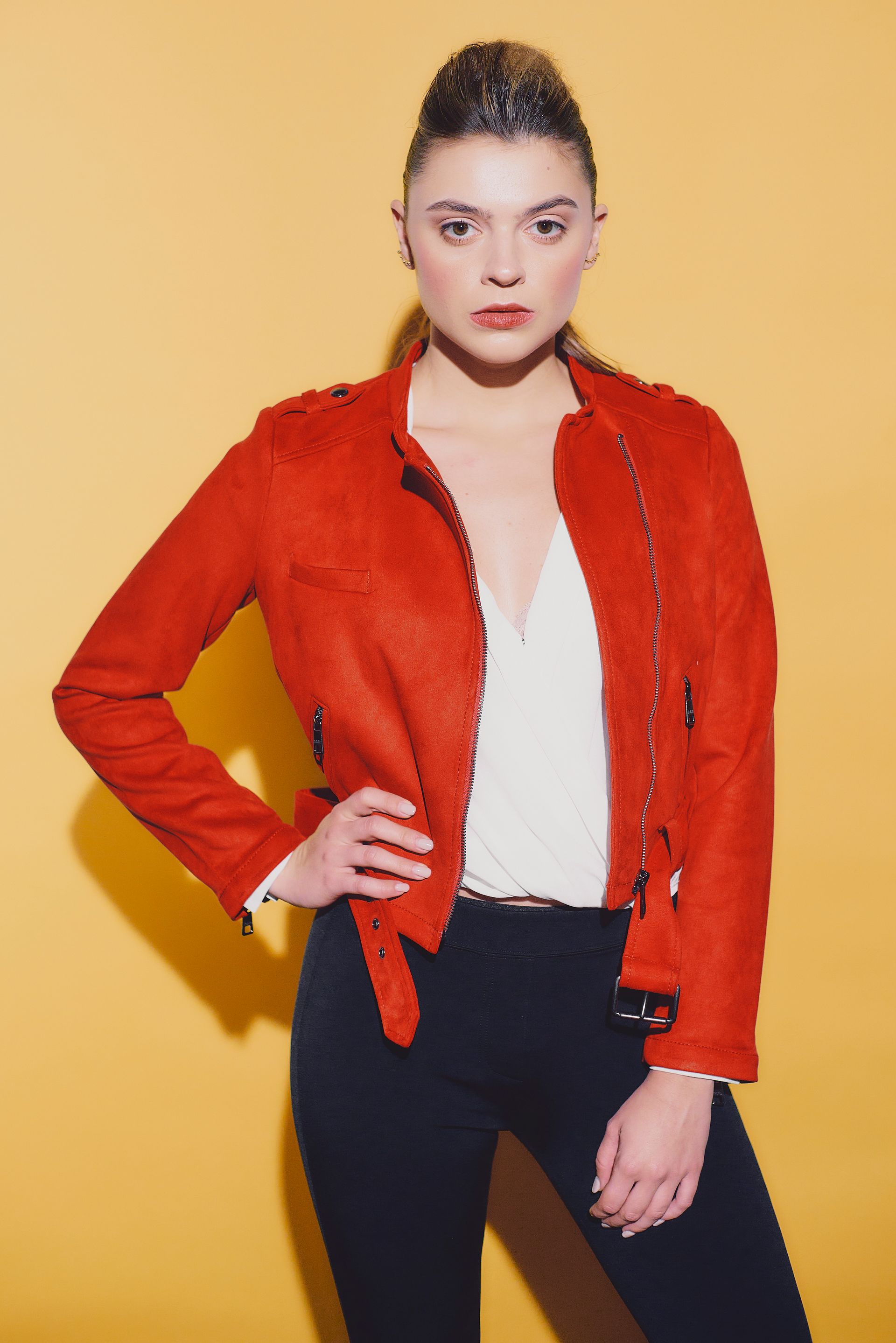A woman wearing a red jacket and black pants is standing in front of a yellow wall.