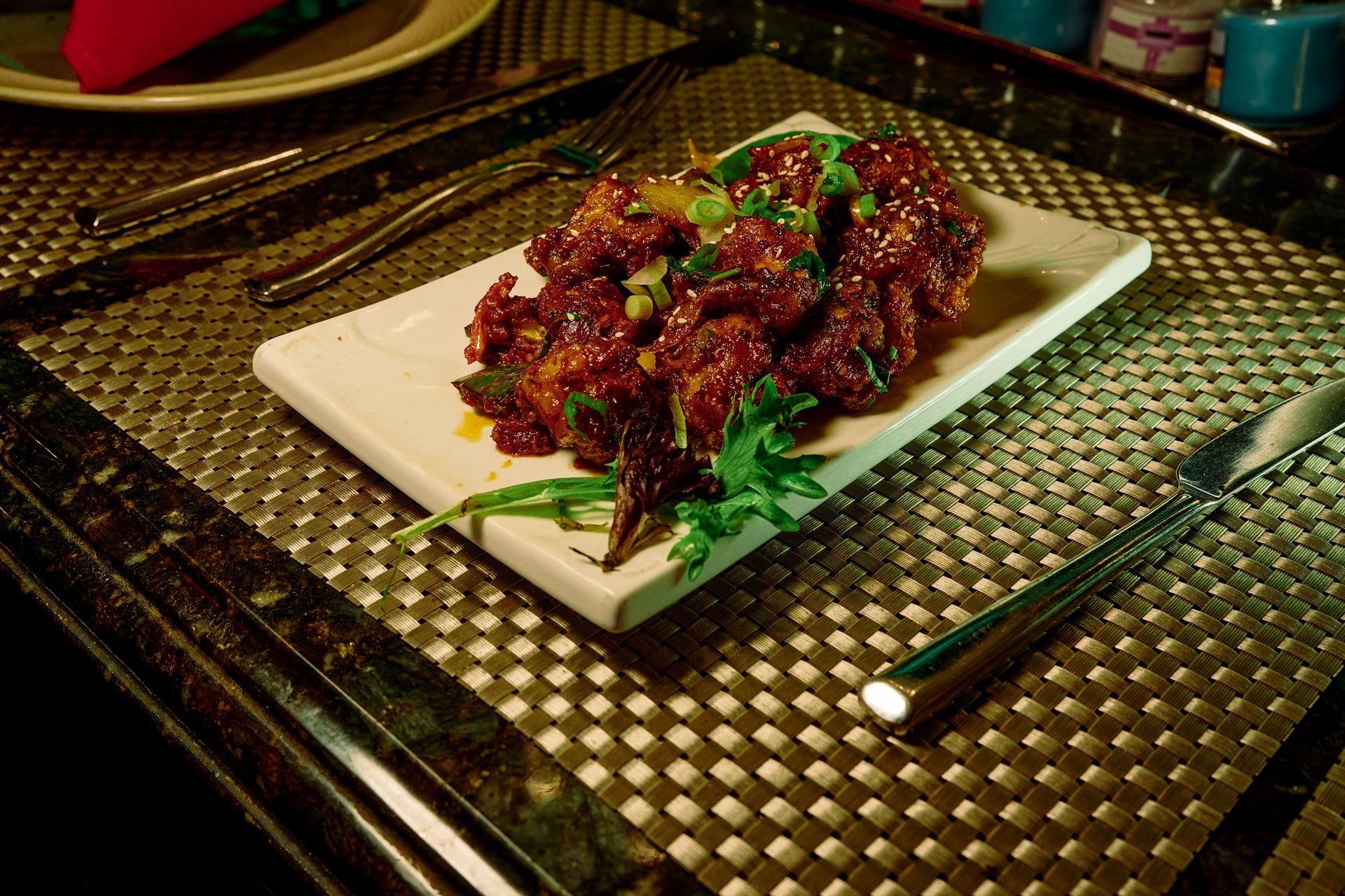 Plate of reddish-brown, saucy fried food garnished with green herbs, served on a white rectangular plate.