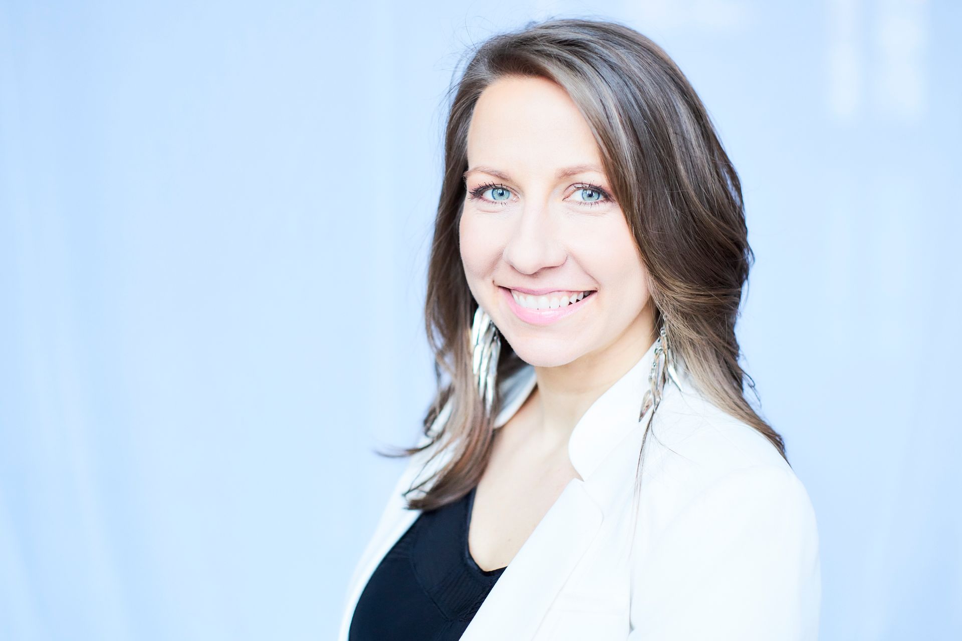 A woman wearing a white jacket and earrings is smiling for the camera.