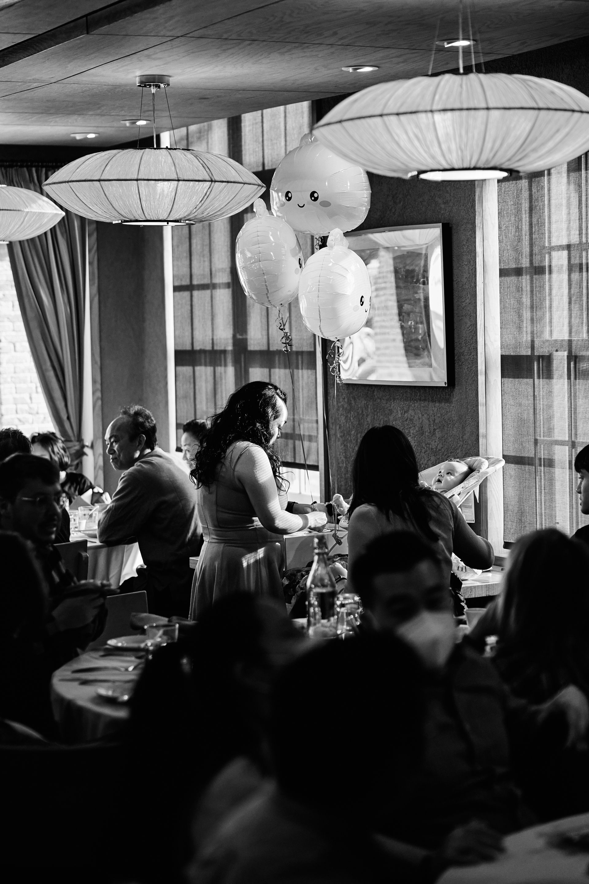 Restaurant interior with people seated at tables, balloons, and pendant lights.