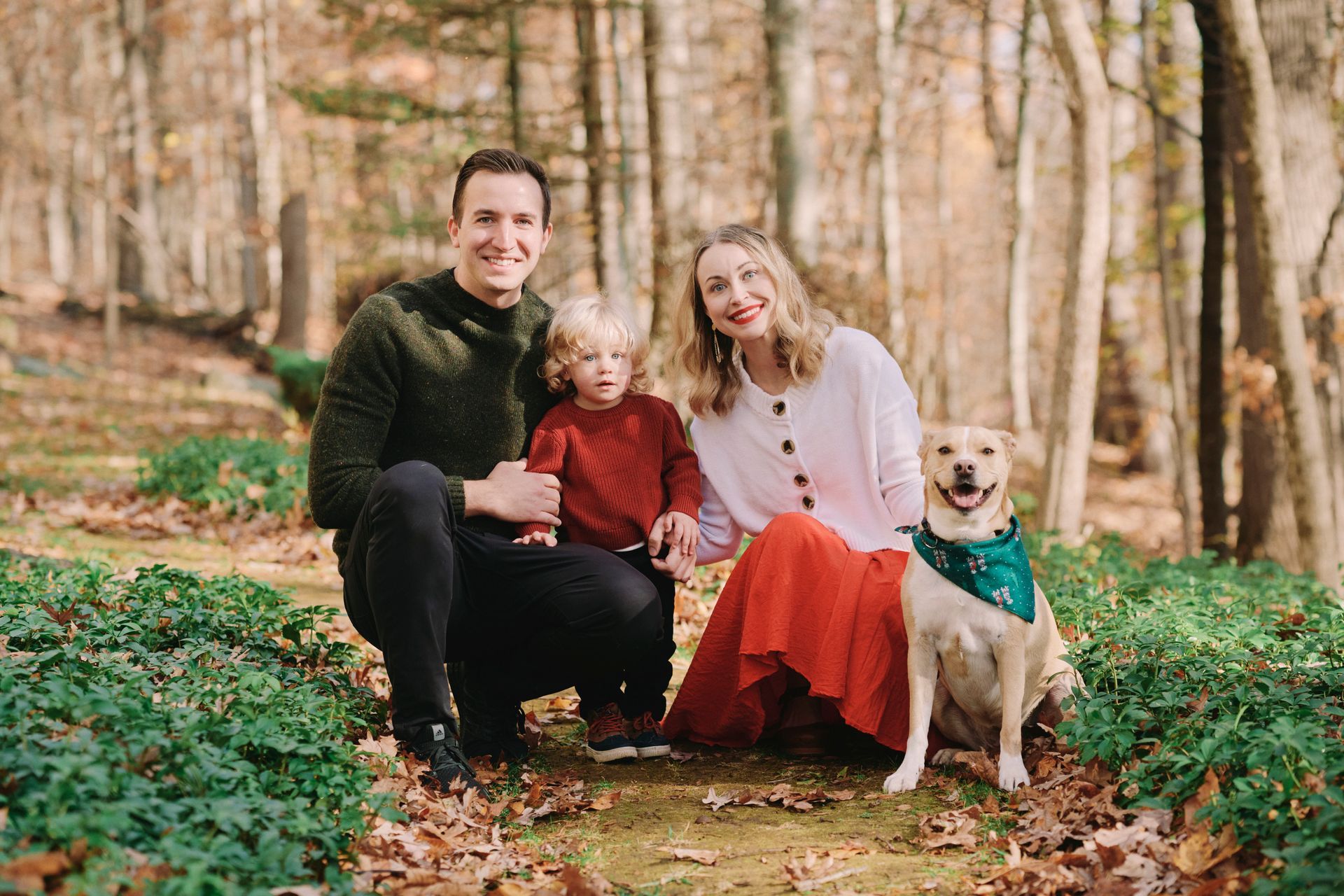 Family of four and dog posing in a forest: man, woman, child, happy dog. Autumn colors.