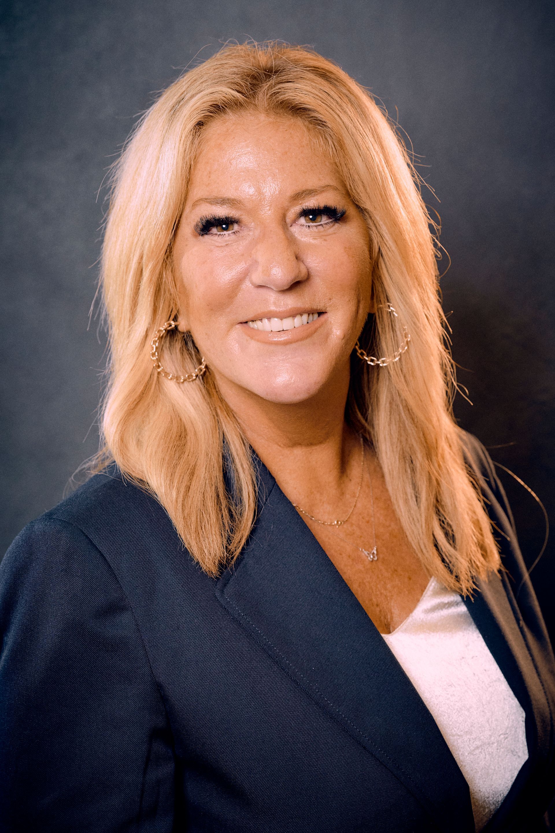 A woman in a blue jacket and white shirt is smiling for the camera.