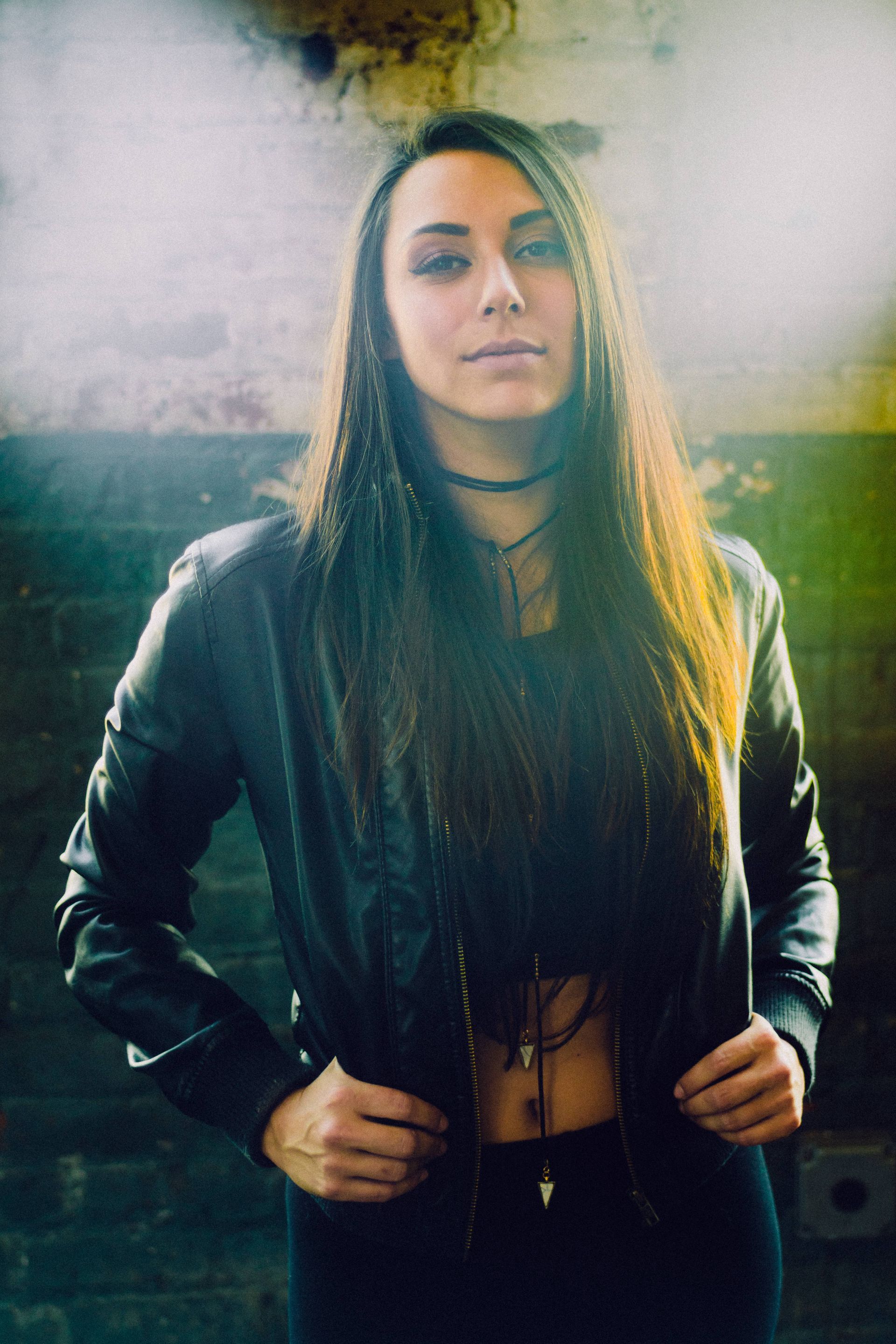A woman in a leather jacket is standing in front of a brick wall.
