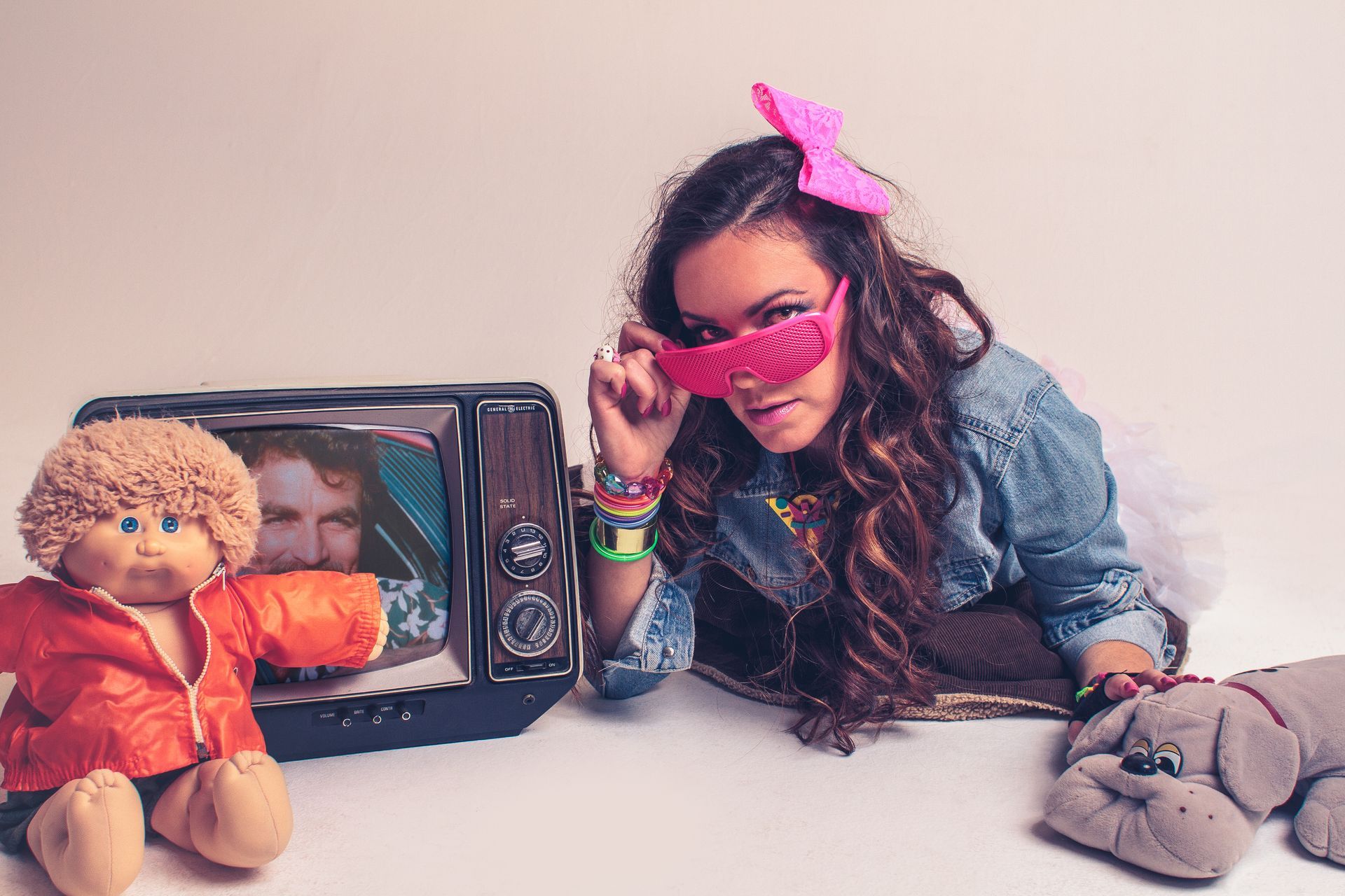 A woman is laying on the floor next to a cabbage patch doll and a teddy bear.