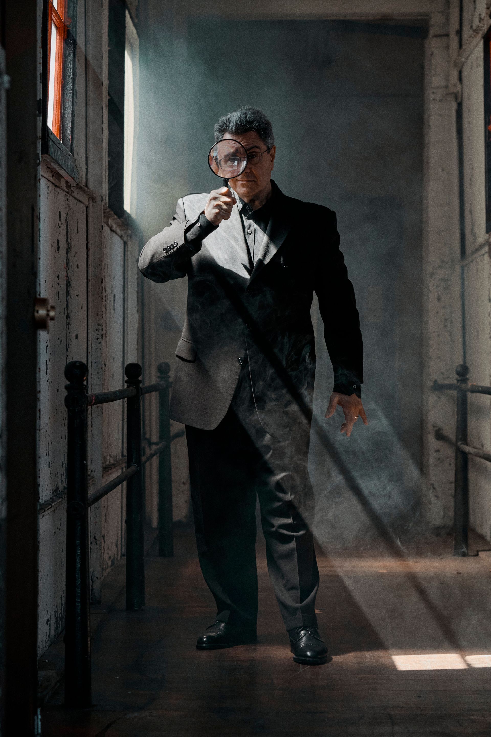 A man in a suit is standing in a hallway with a magnifying glass.