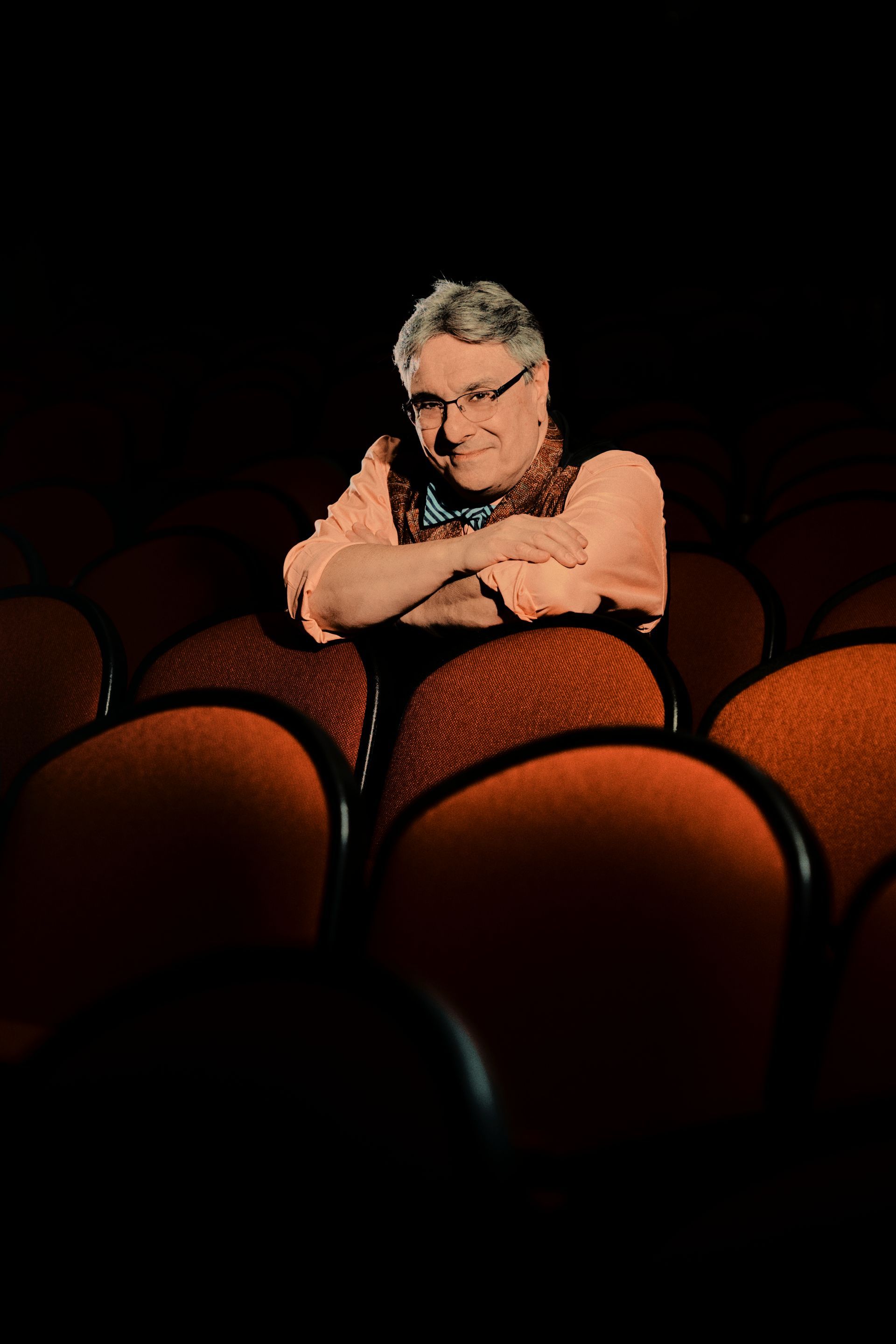 Man in glasses leaning on theater seats, smiling.