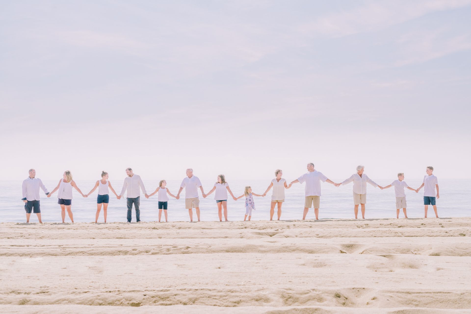 Group of people holding hands on a beach, wearing white shirts and various shorts.