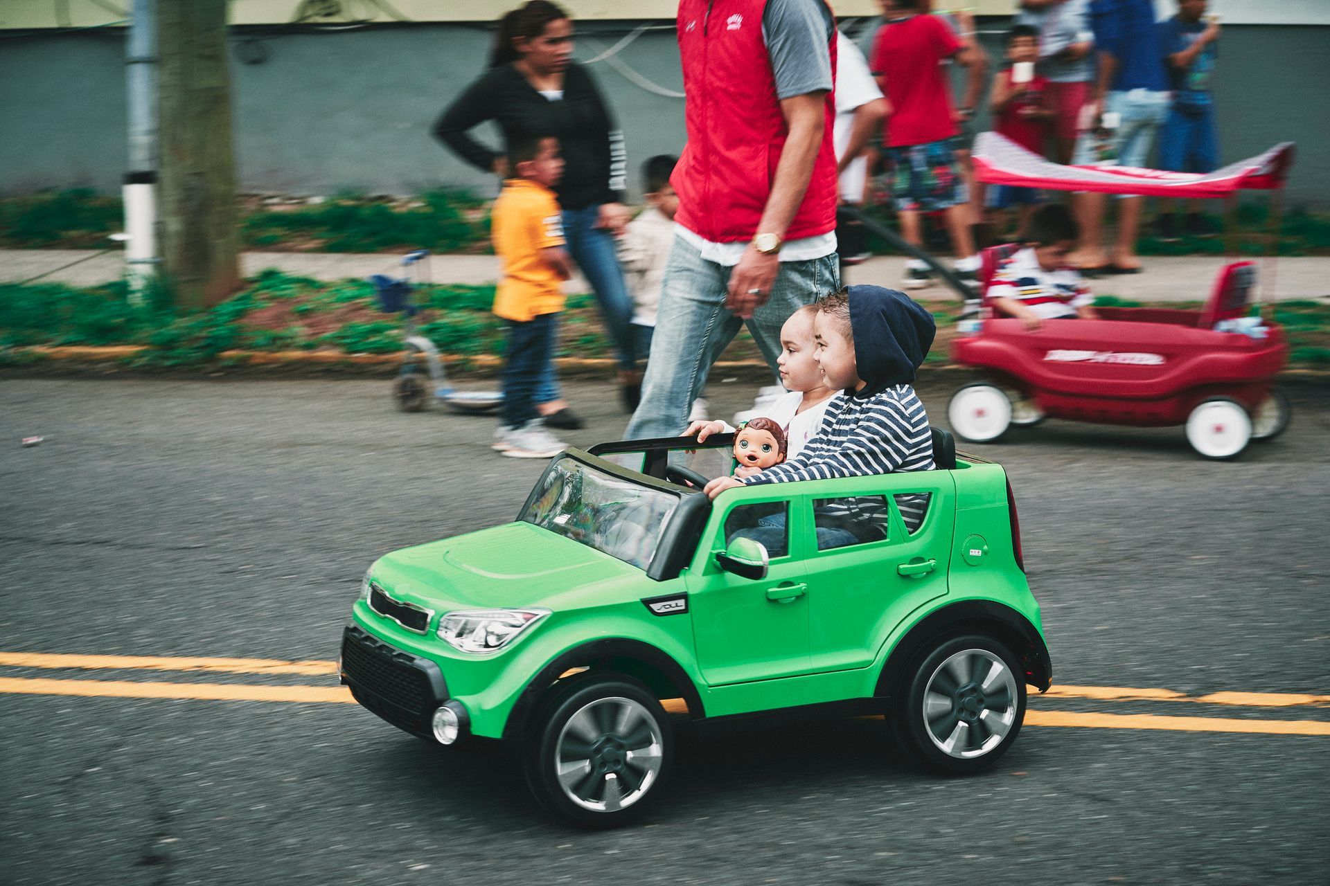A man is holding a baby in a green toy car.