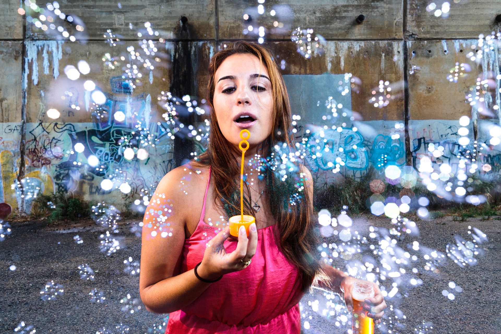A woman in a pink dress is blowing soap bubbles.