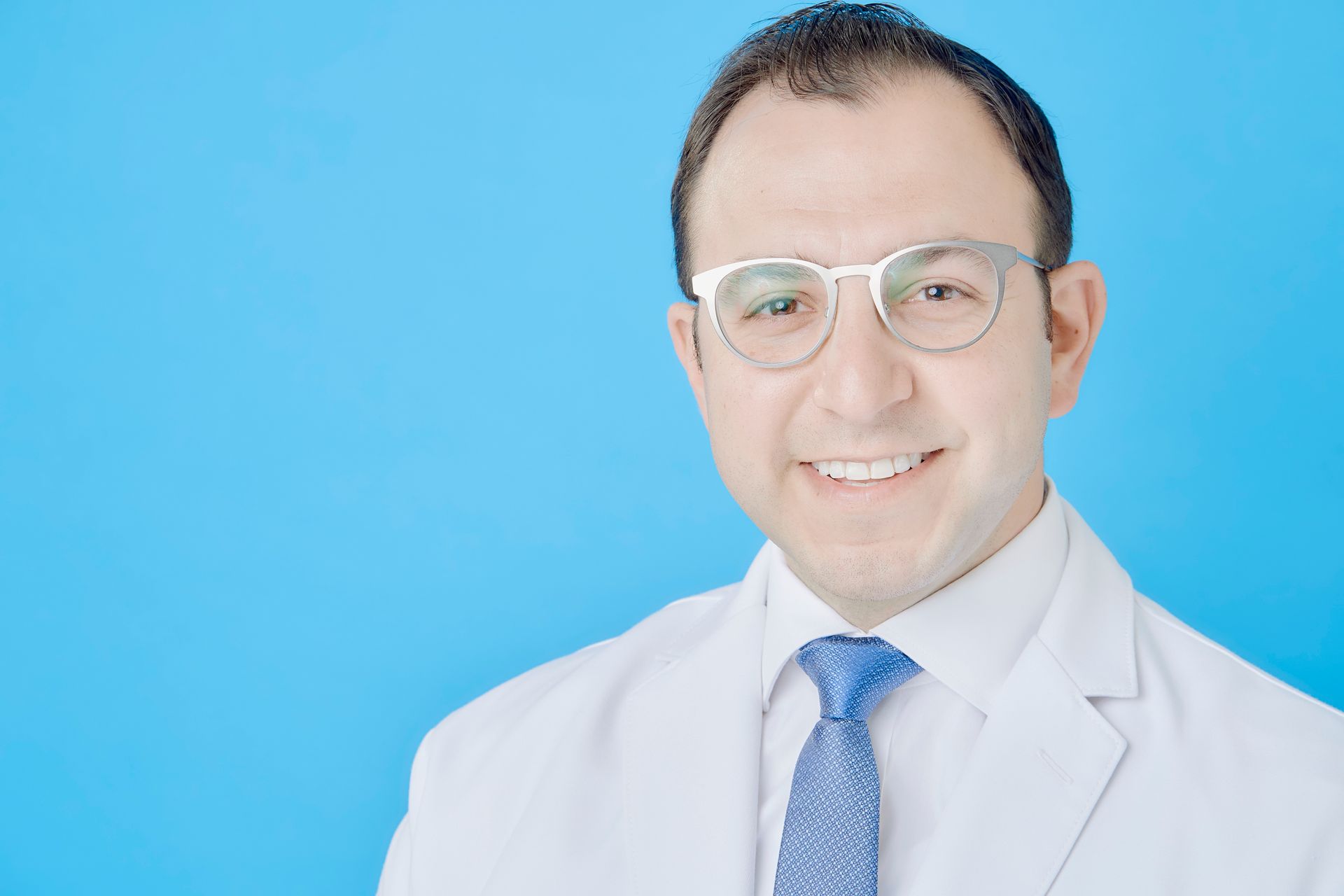 A man wearing glasses and a white coat and tie is smiling for the camera.