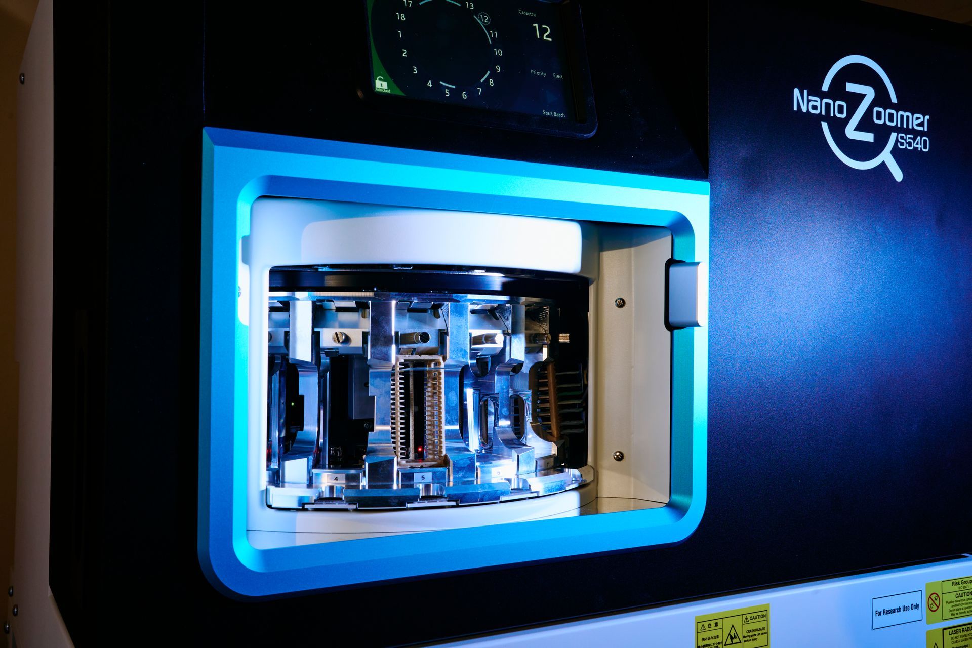 A close-up of a NanoZoomer 2.0-HT slide scanner, black and teal, with internal components visible.