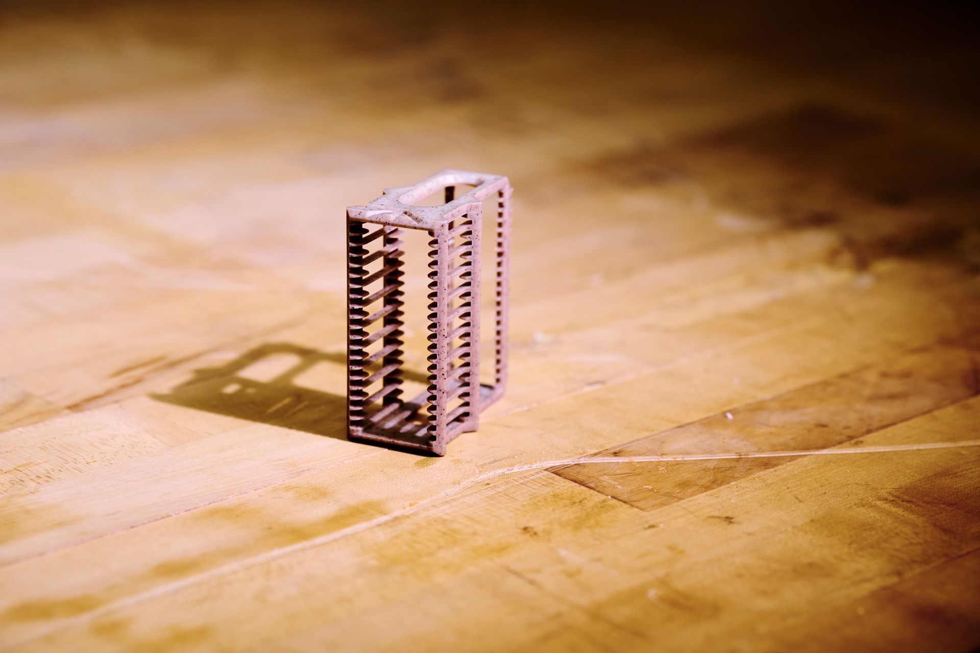 A small white plastic gear-like object standing on a sunlit wooden floor, casting a shadow.