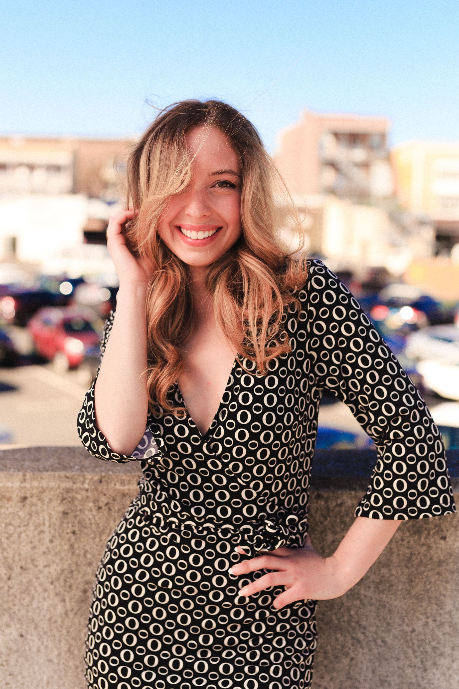 A woman in a black and white dress is standing next to a wall and smiling.