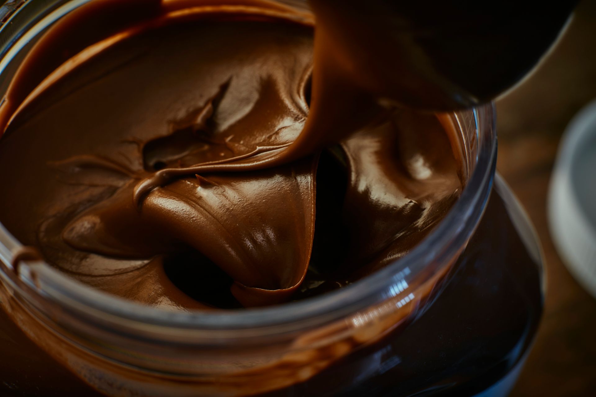 Jar of chocolate hazelnut spread, spoon scooping out a swirl of creamy, rich brown product.