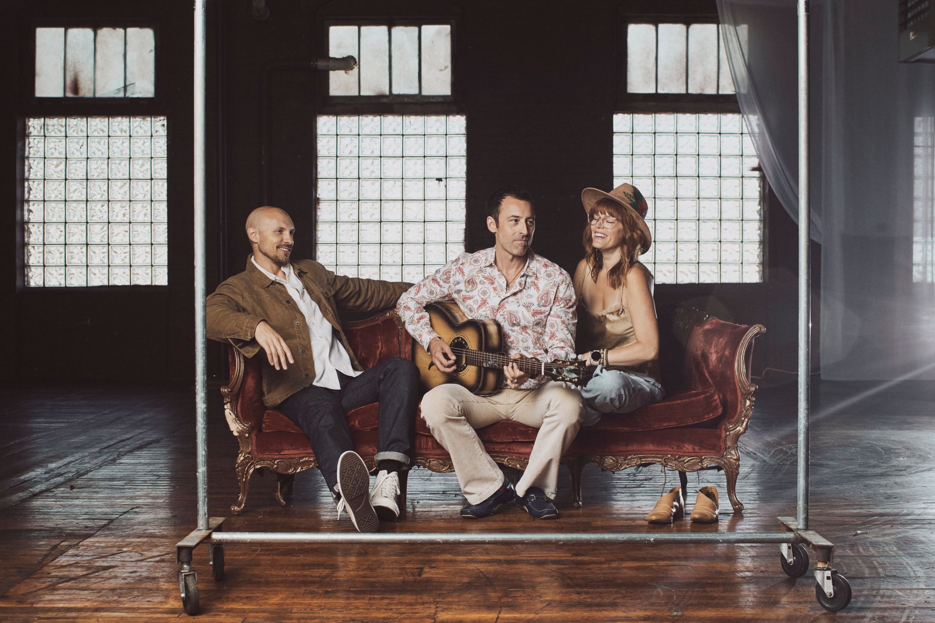 Three people are sitting on a couch playing guitars.