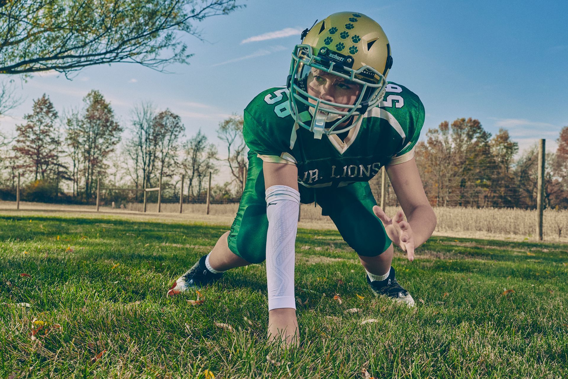 Football player in green crouches at the line on a grassy field, helmet on, ready to start the play.