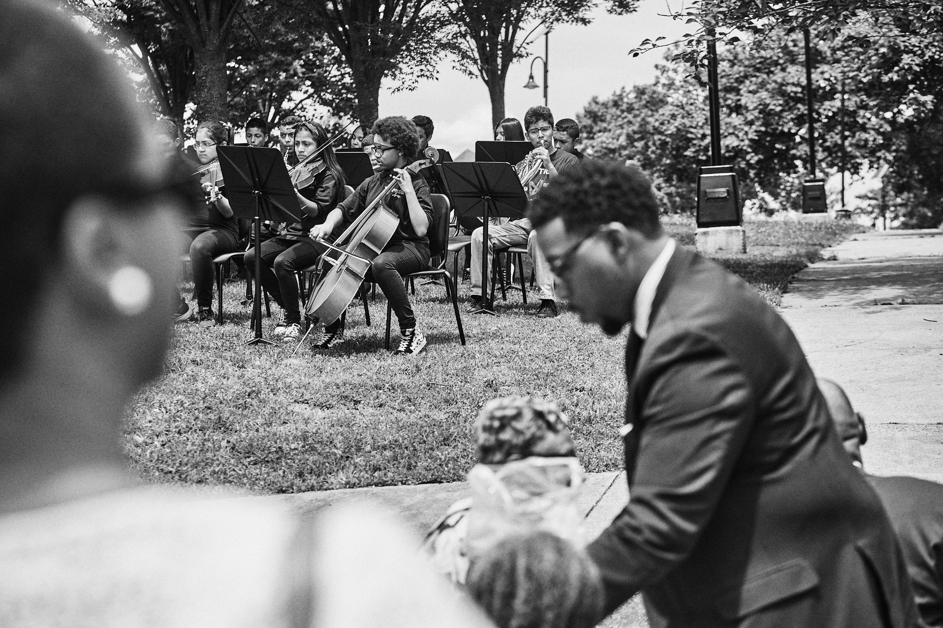 A man in a suit is standing in front of a group of people playing instruments in a park.