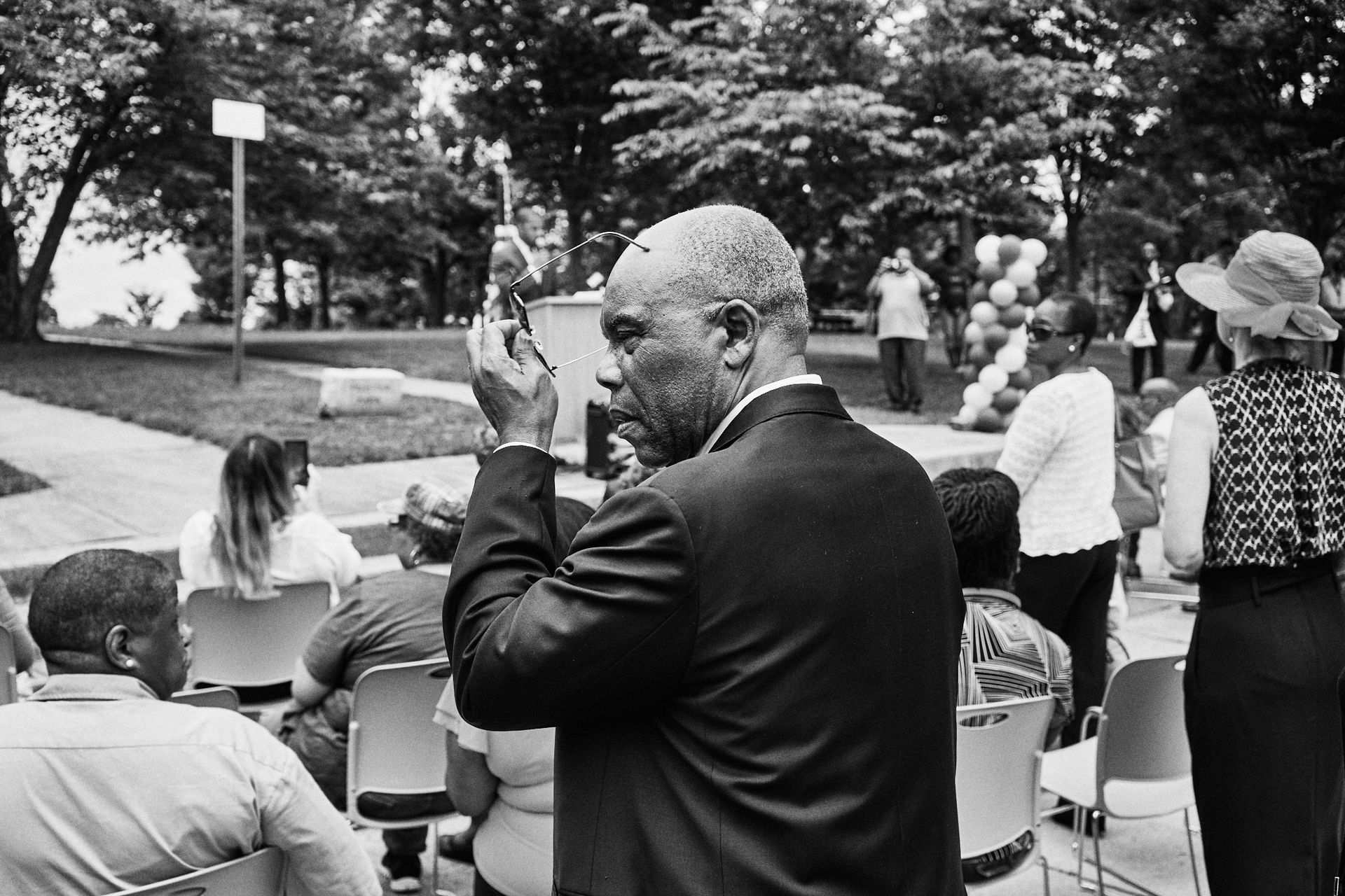 A man in a suit is taking a picture of a group of people in a park.