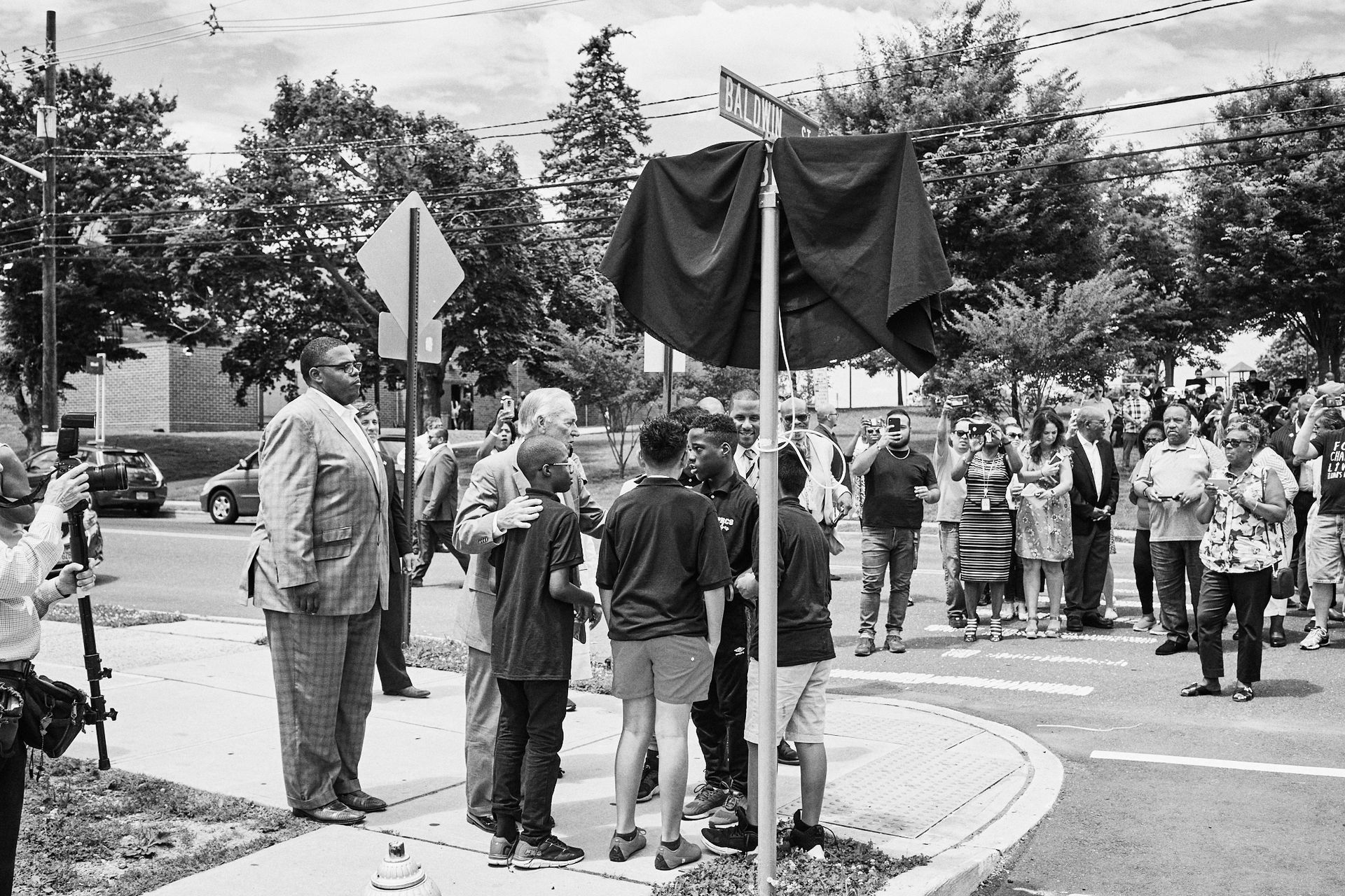 A black and white photo of people standing around a street sign