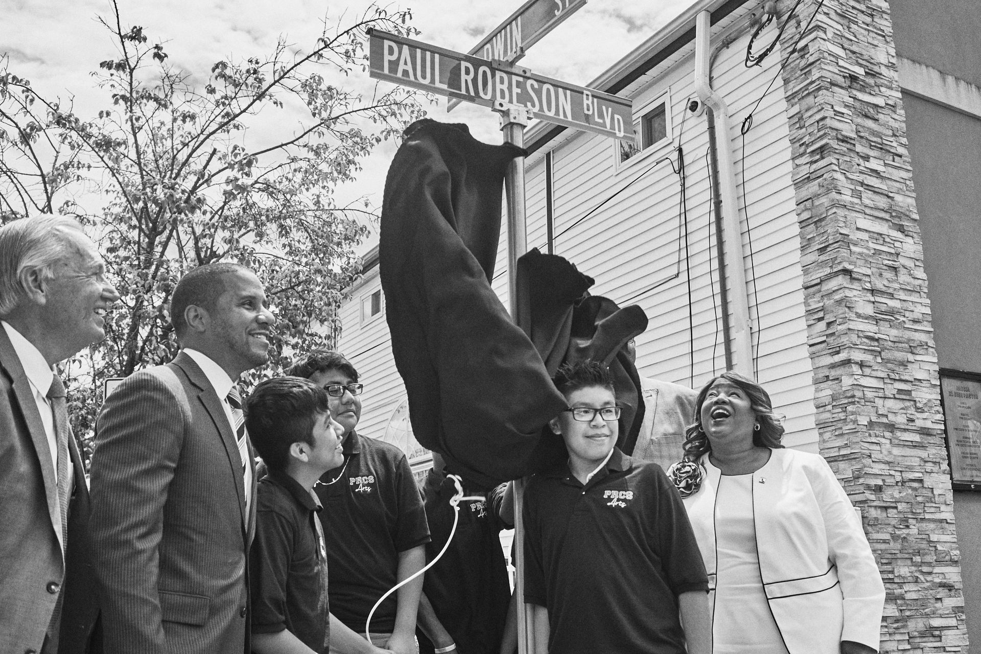A group of people are standing around a street sign that says paul robeson ave.