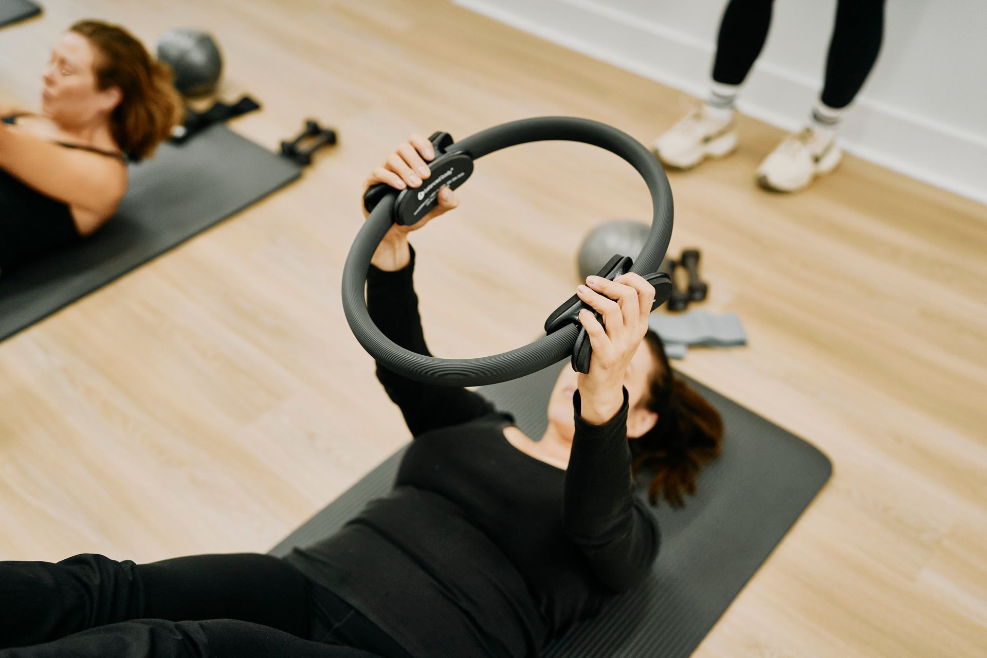 People exercising on yoga mats, lifting a ring-shaped fitness prop in a studio