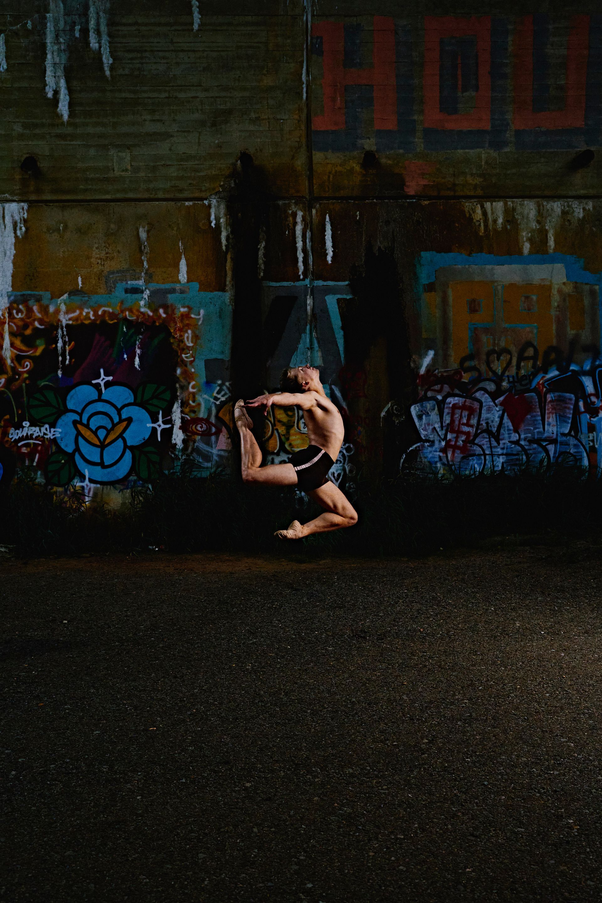 Person upside down in a yoga pose against a graffiti-covered wall in a dark urban setting
