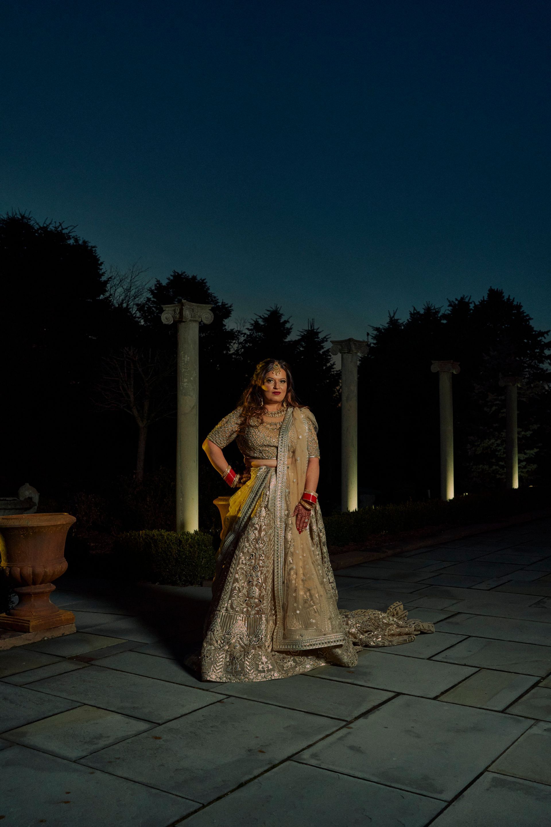 A woman in a long dress is standing in front of a fountain at night.