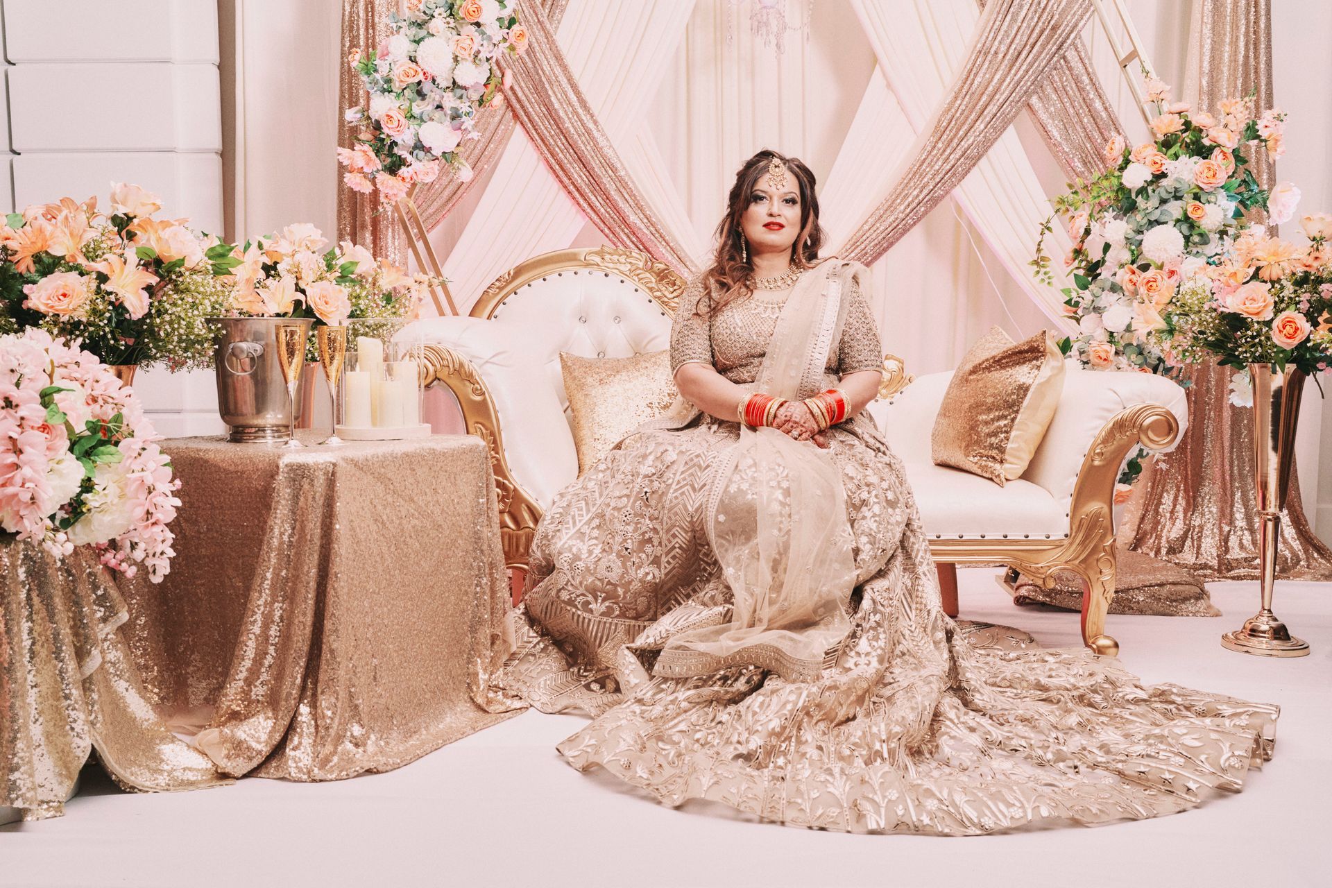 A woman in a long gold dress is sitting on a couch.