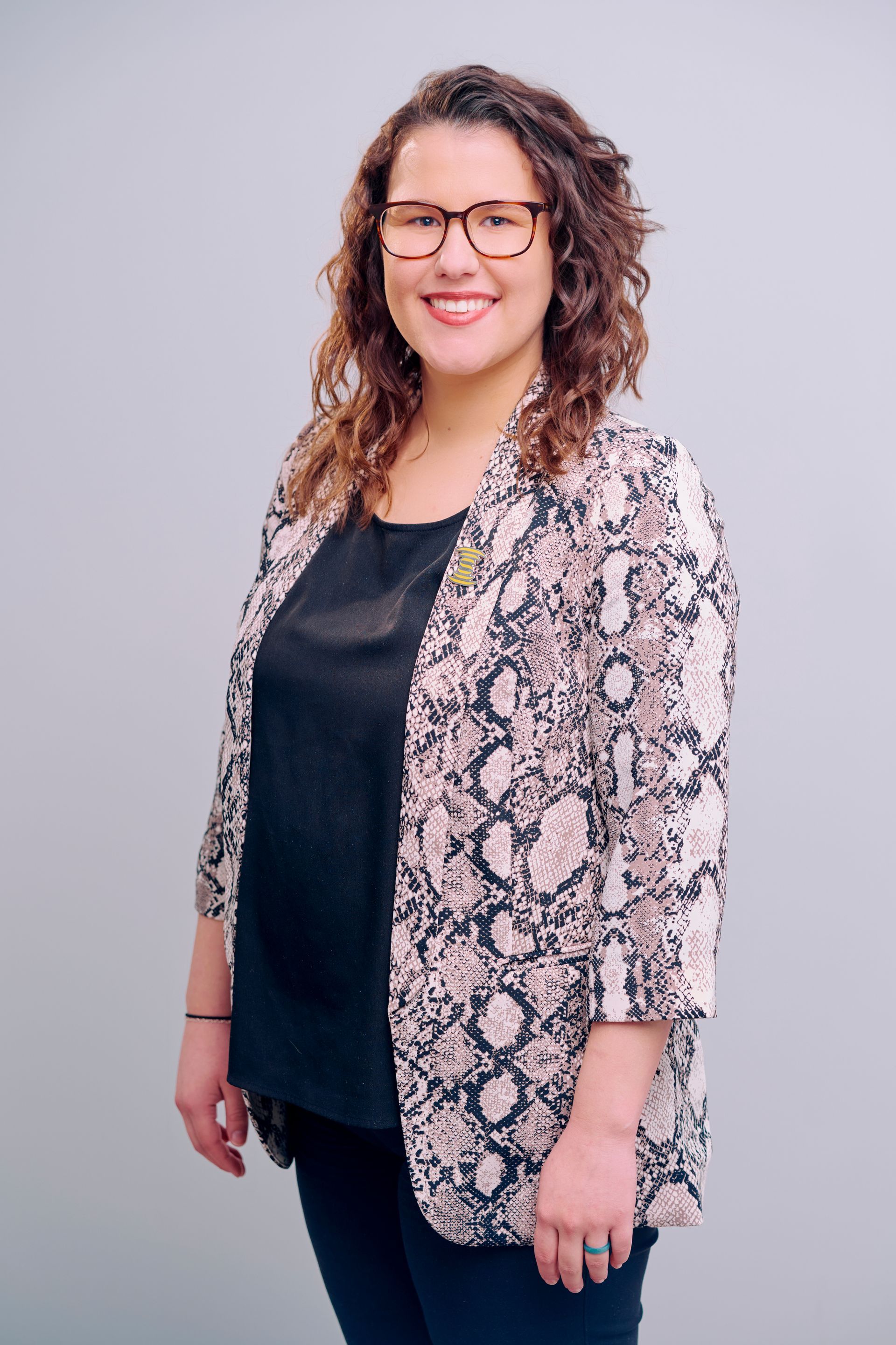 Woman with curly brown hair, glasses, and a patterned blazer smiles.