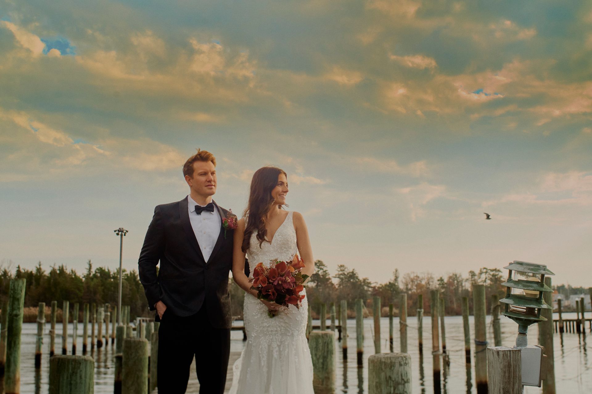 A bride and groom are standing next to each other on a dock.