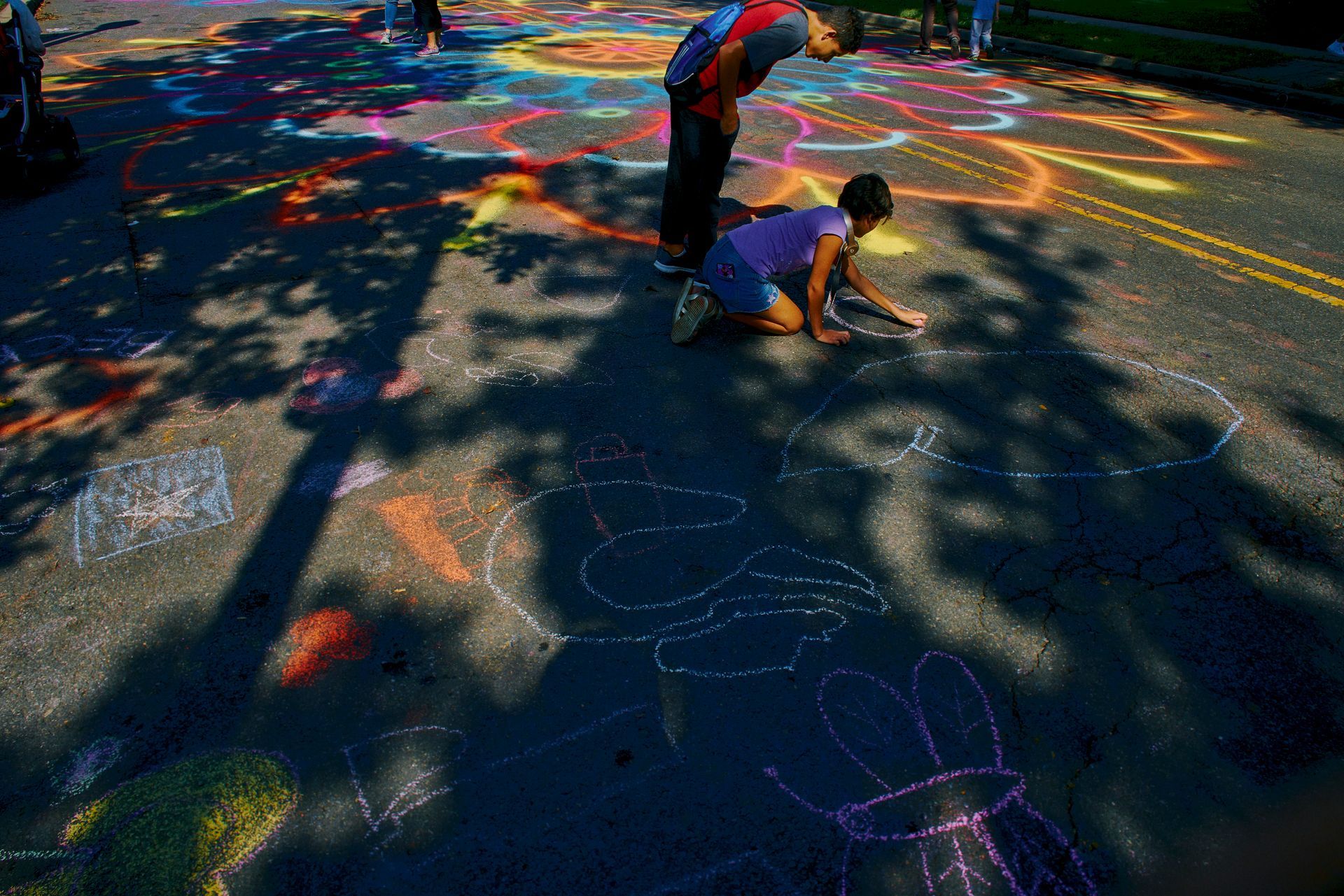 A man and a woman are drawing with chalk on the street.