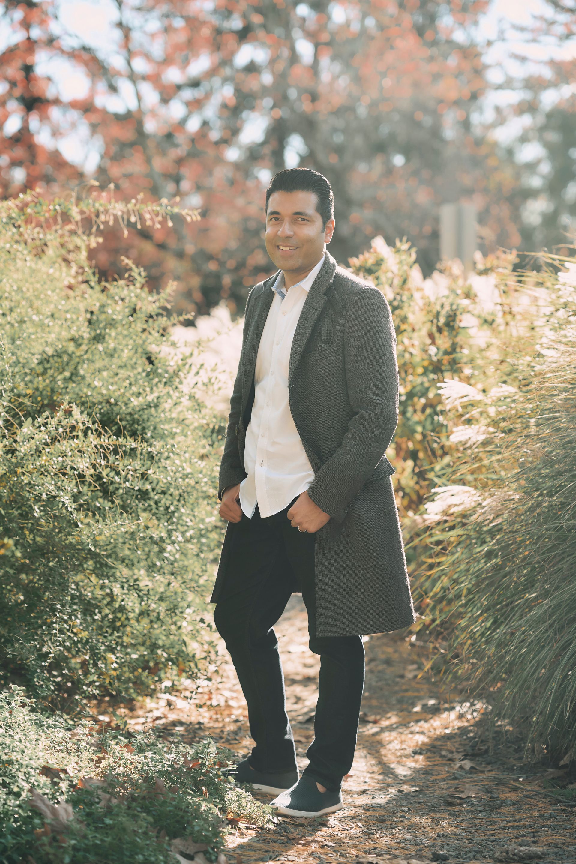 A man in a suit and coat is standing in a park.