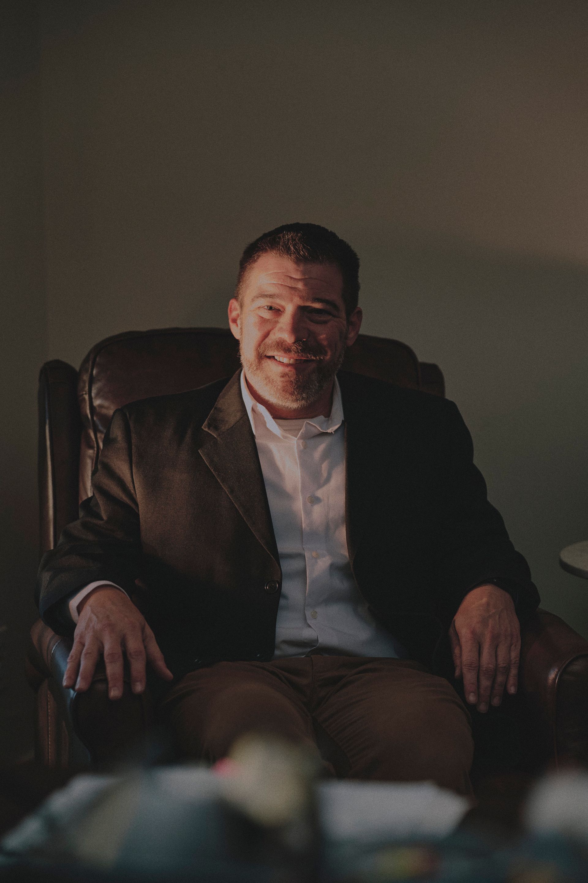 A man in a suit is sitting in a chair and smiling.